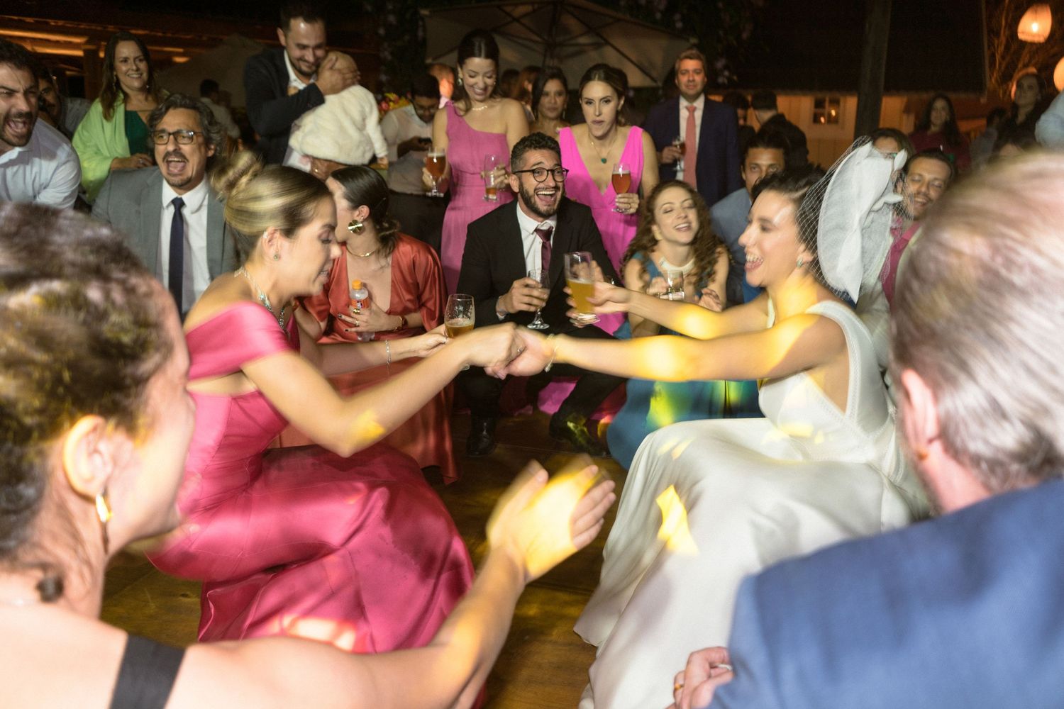 Convidados do casamento dançam na pista junto com a noiva e aproveitam a música e luzes coloridas. Fotografia documental e em movimento