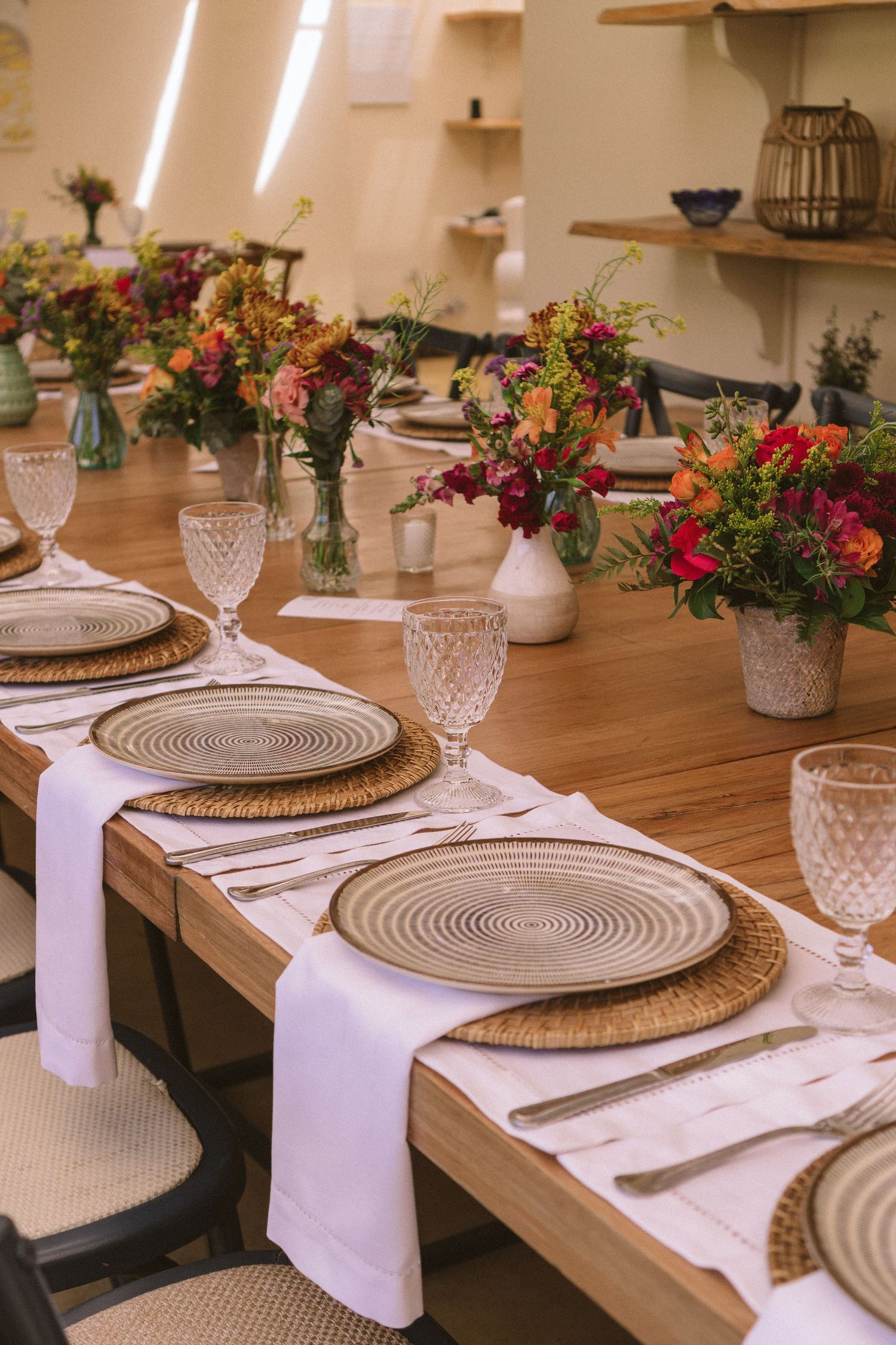 Mesa posta elegante com detalhes em tecido, cristais e arranjos florais coloridos em vasos de cerâmica branca