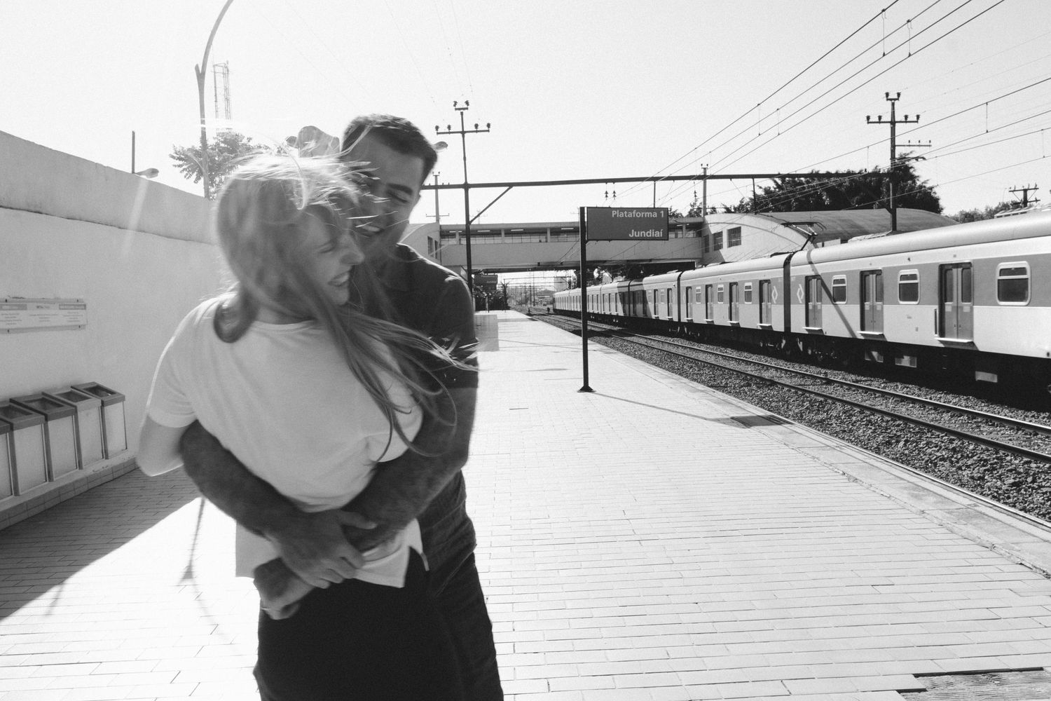 Casal se diverte e ri enquanto se abraça numa estação de trem © Clara e Matheus Fotógrafos de Casamentos