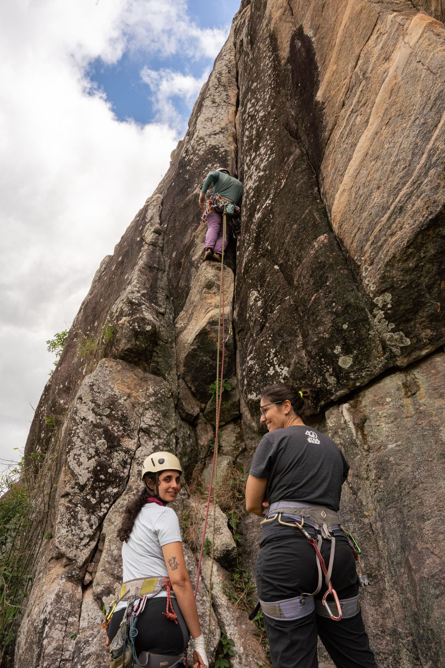 Escaladores subindo uma parede rochosa íngreme usando equipamentos de segurança e arneses.