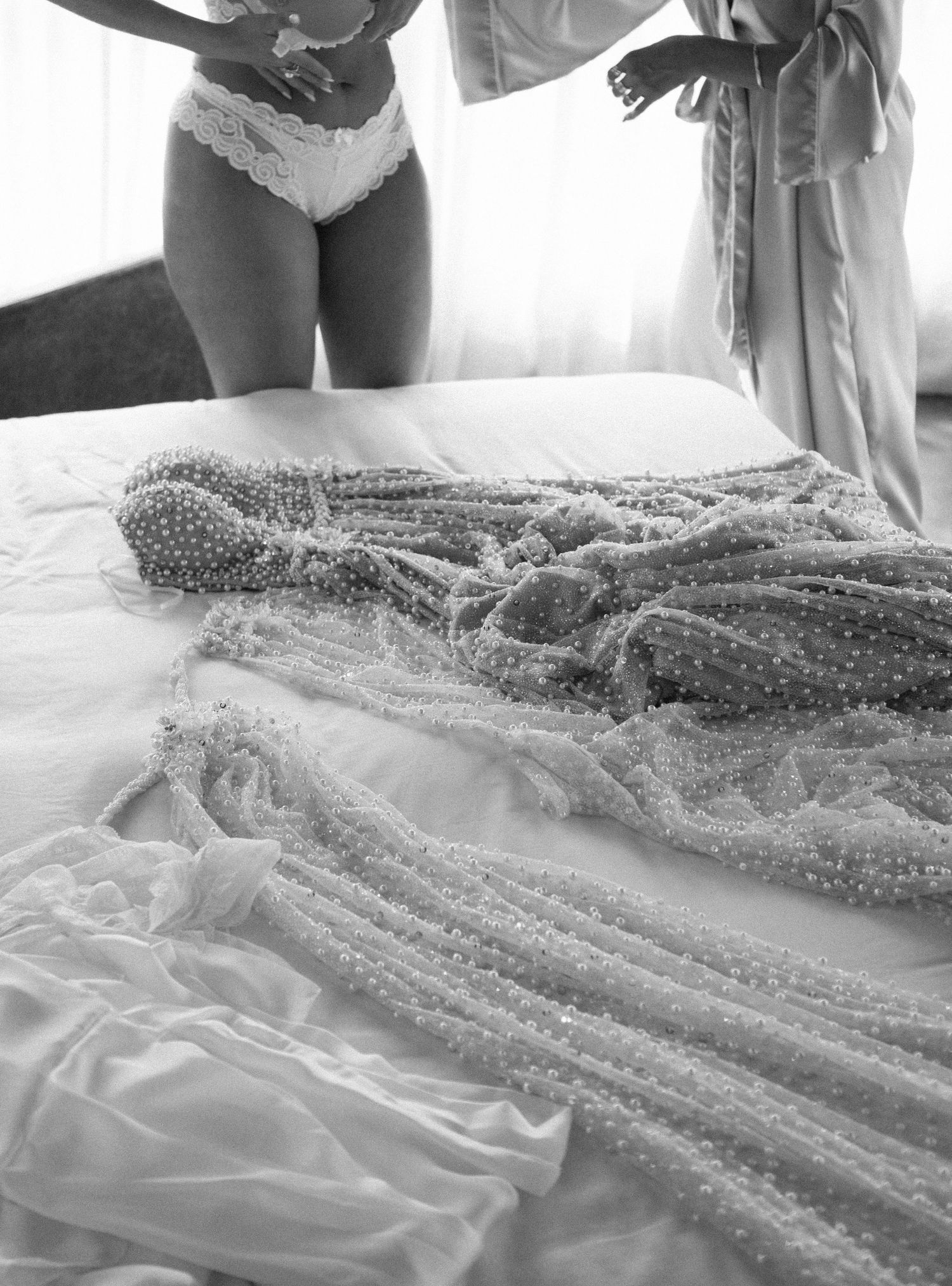 Noiva se prepara para cerimônia de casamento em suas roupas íntimas com vestido sobre a cama © Clara e Matheus Fotógrafos para Casamentos
