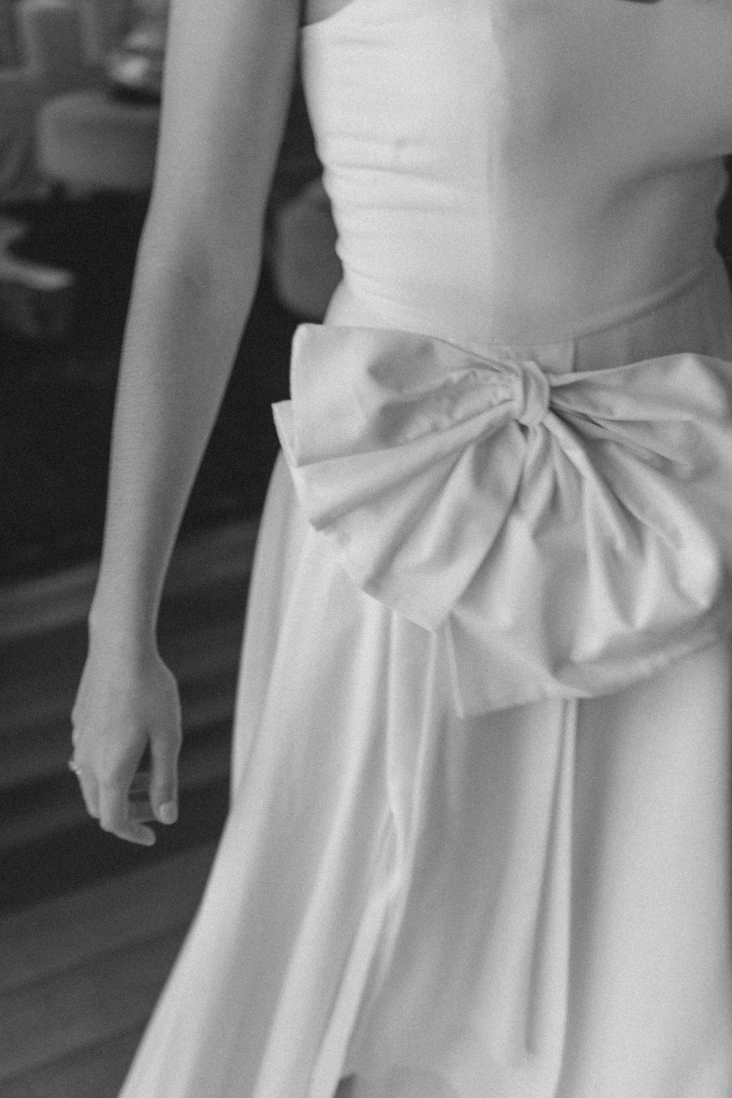 Detalhe de close-up de vestido de noiva branco com laço elegante e oversized na cintura, criando um caimento gracioso