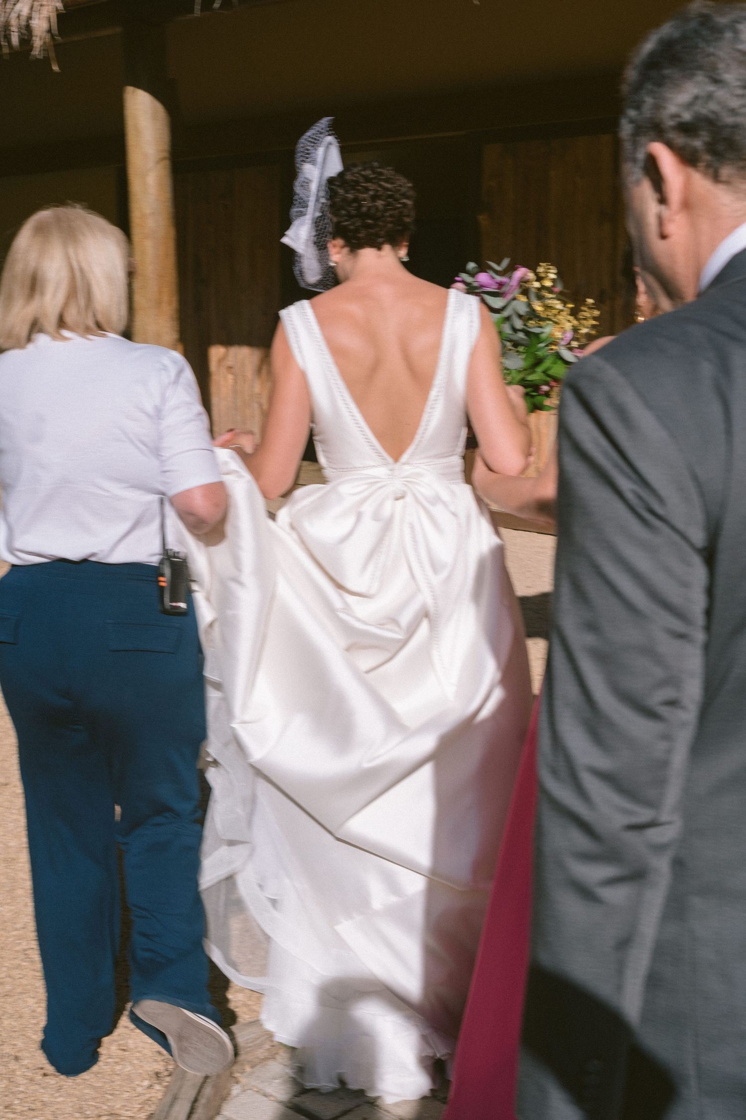Vestido de noiva com design de costas em V profundo visto de trás, sendo guiada para a cerimônia de casamento