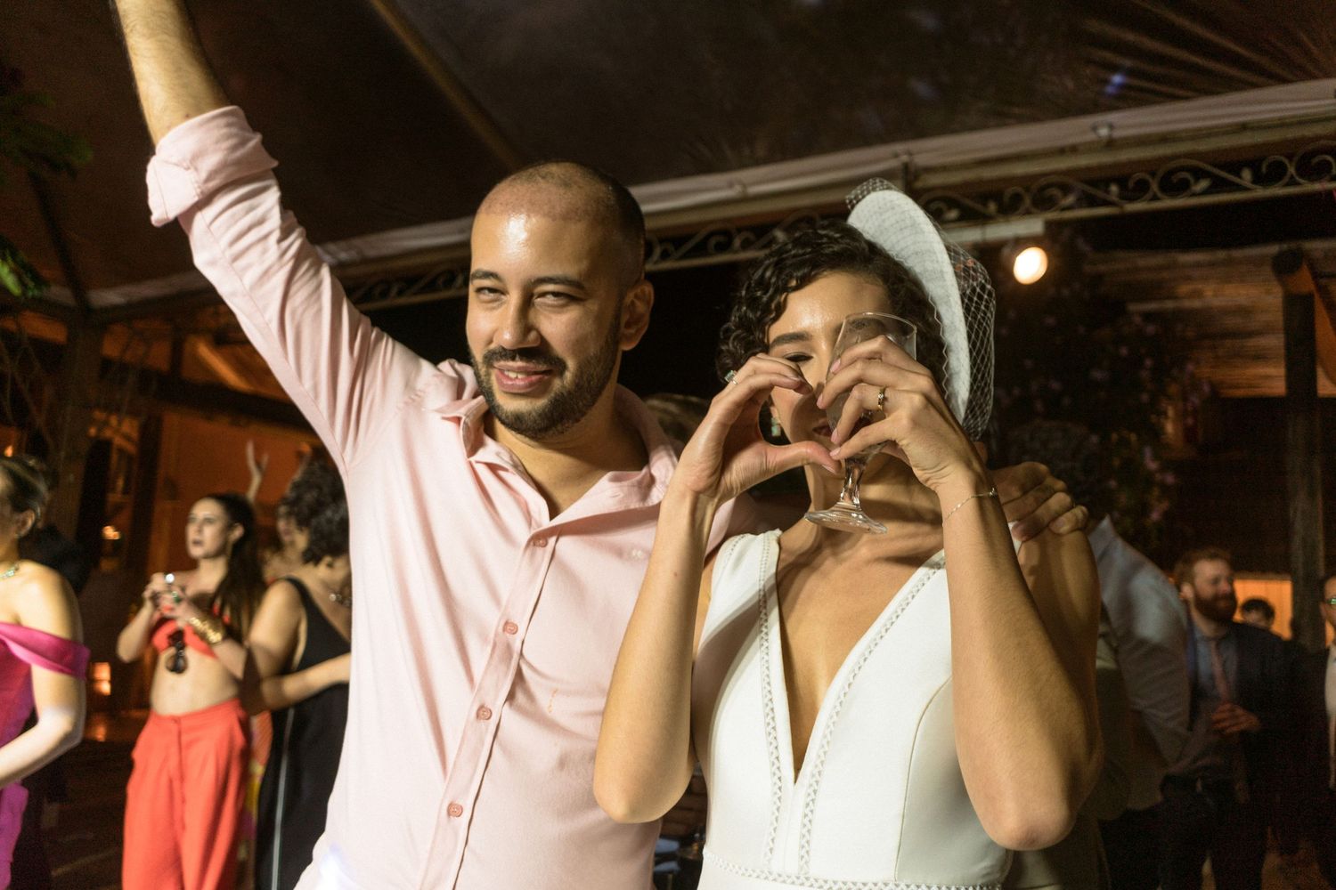Noiva faz um coração com as mãos para os fotógrafos de casamento Clara e Matheus durante a festa de casamento