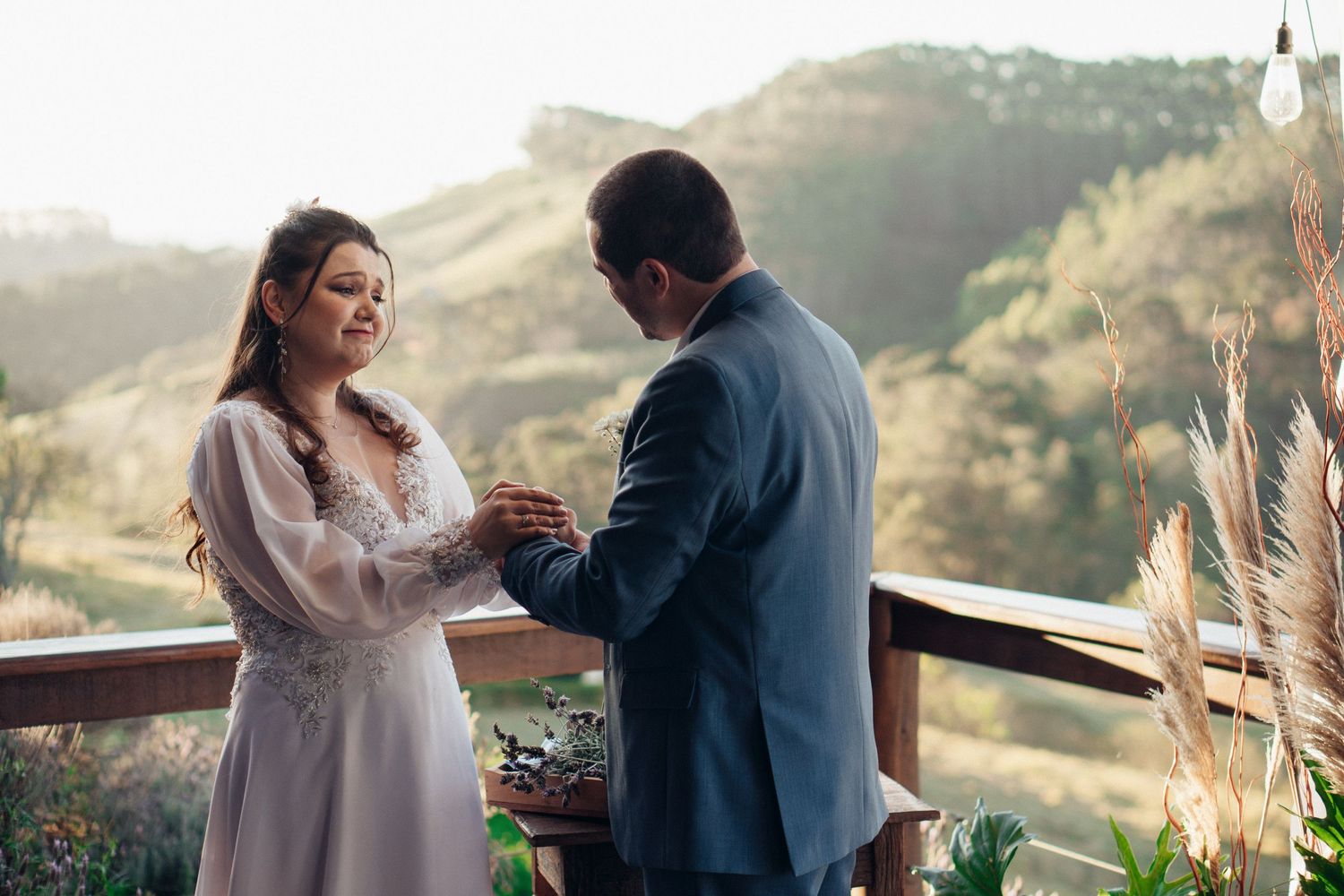 Momento romântico entre um casal em trajes de casamento no deck ao ar livre com montanhas ao fundo.