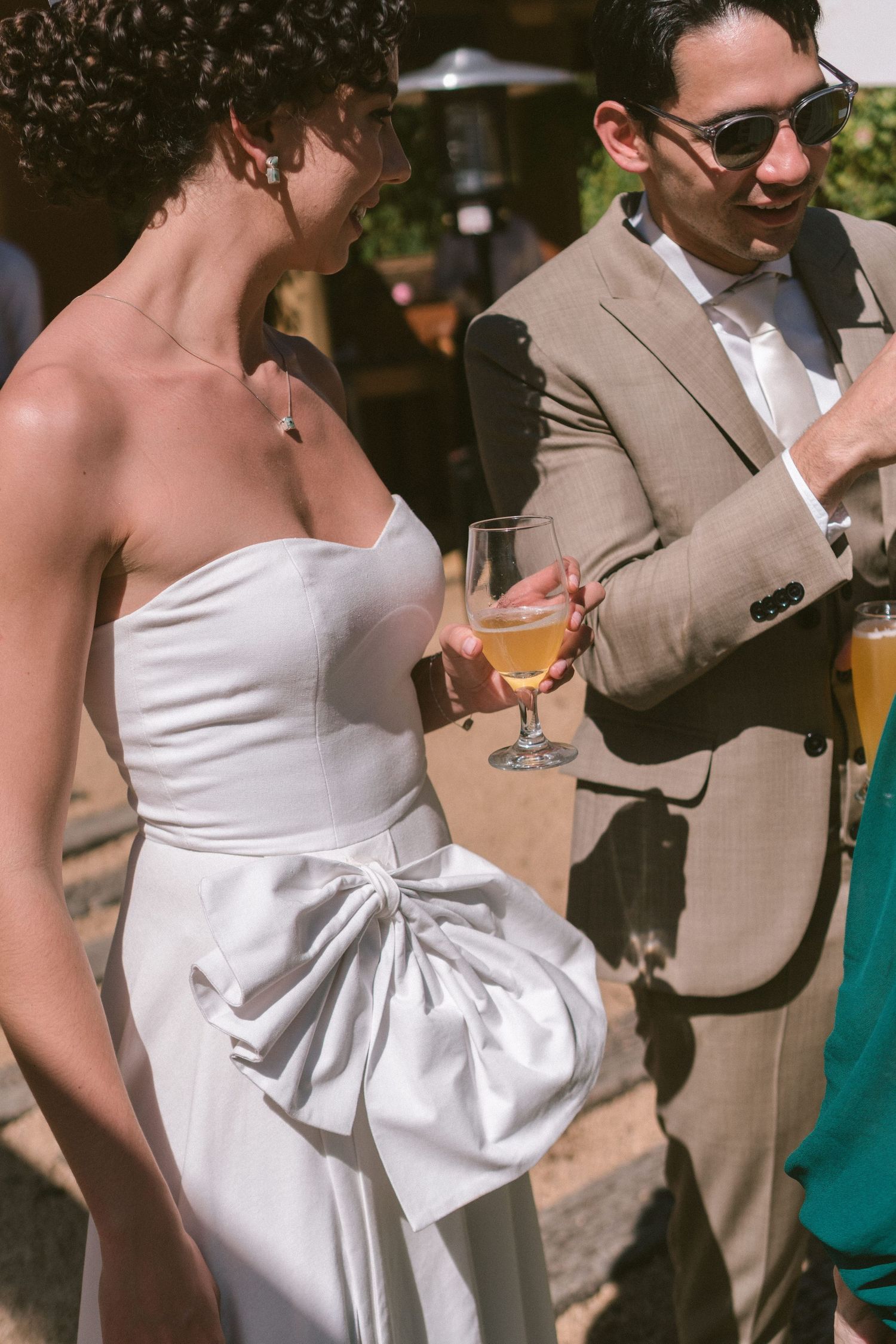 Os noivos tomando cerveja na recepção ao ar livre, com a noiva em vestido branco e laço lateral, fotografia documental