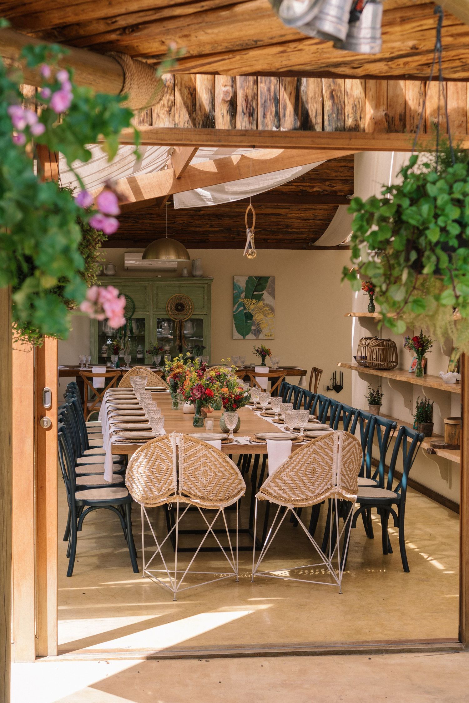 Decoração rústica e aconchegante para casamento: mesa de jantar com cadeiras de tecido, plantas penduradas e vigas de madeira, perfeita para