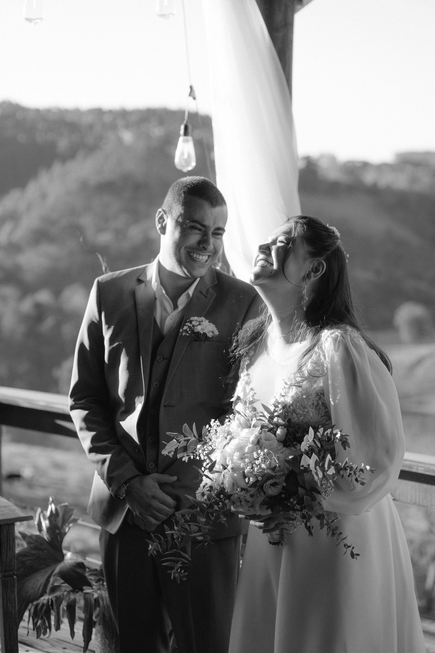 A joyful black and white wedding portrait on a scenic outdoor balcony.