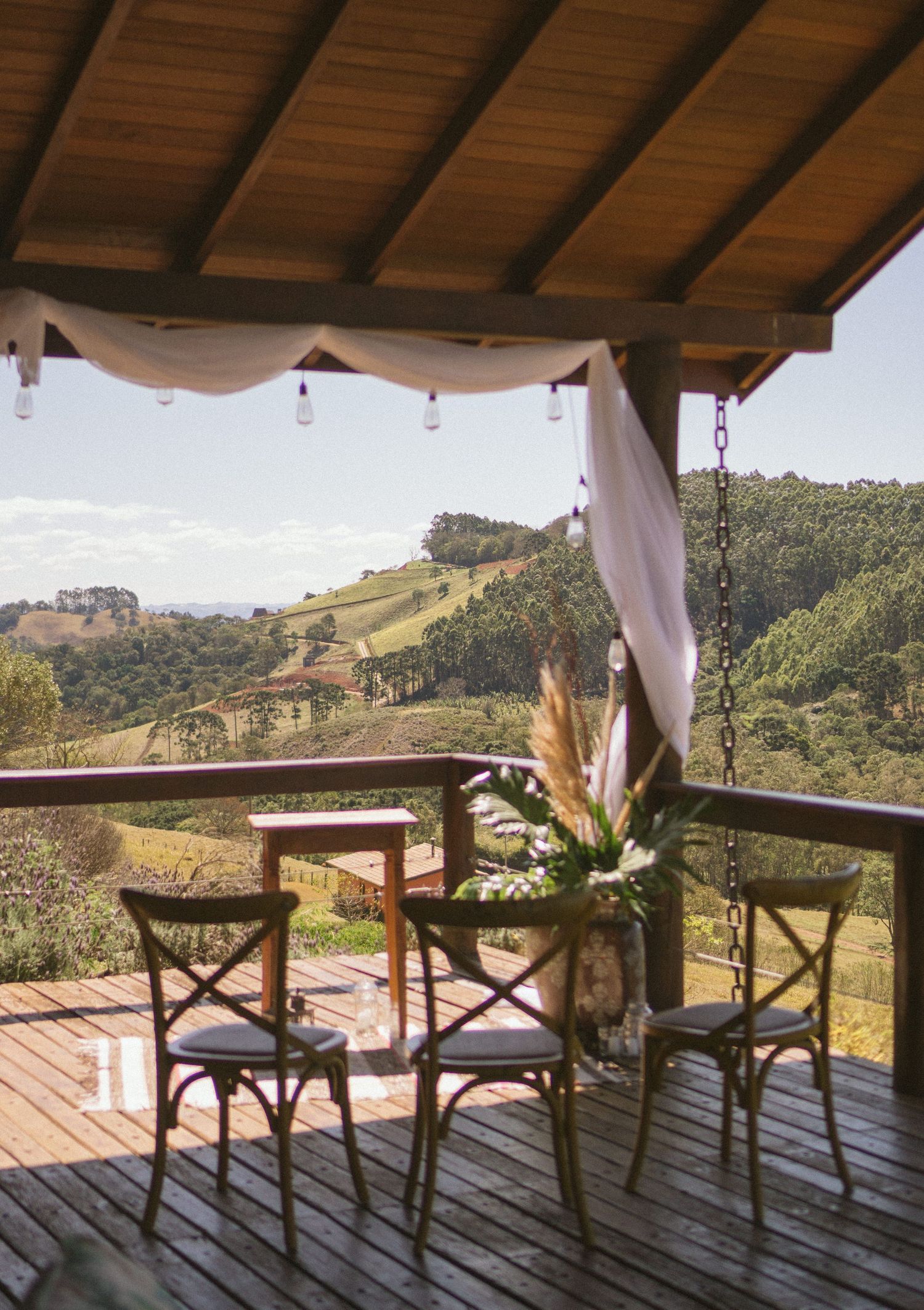Covered deck with white draping and bistro chairs overlooking a scenic mountain landscape.