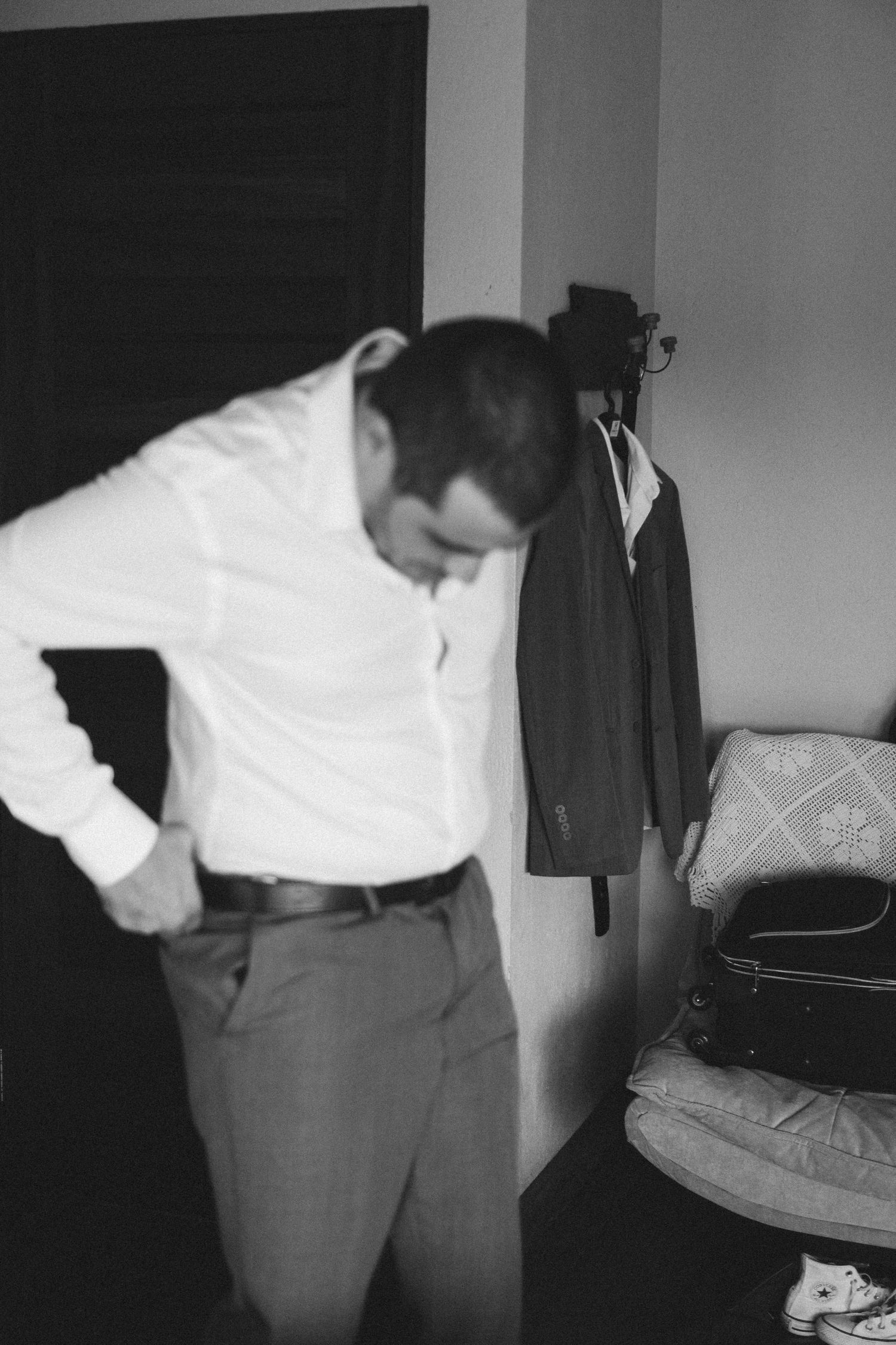 A person in formal white shirt and gray pants getting dressed in a bedroom.