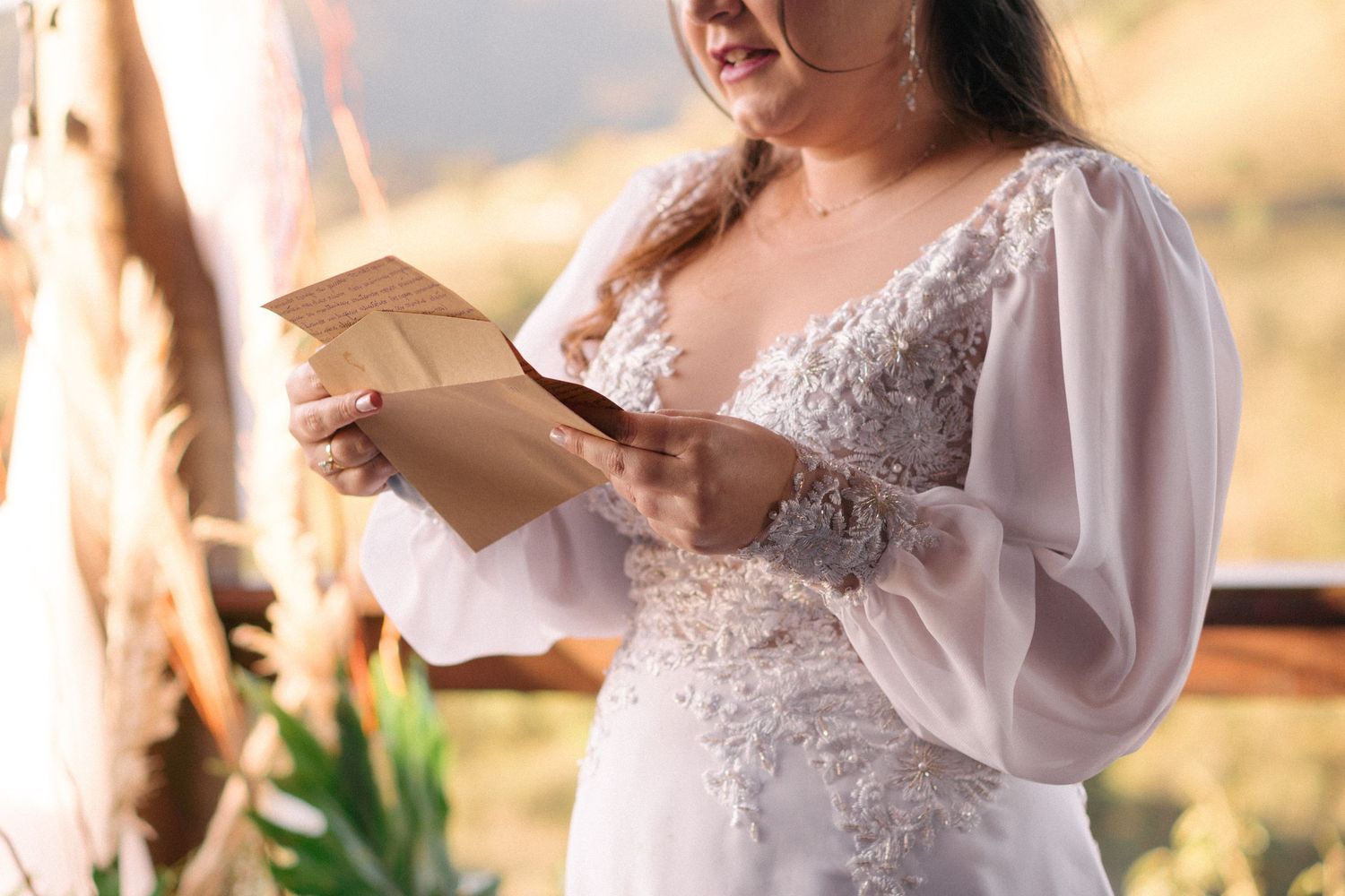 Detail shot of a bride in a white lace dress with billowing sleeves reading a letter.