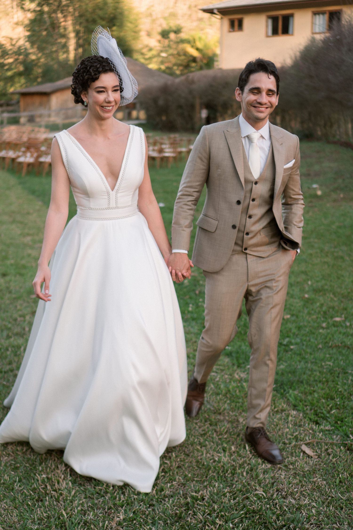 Elegant couple walking on grass in wedding attire featuring a flowing white dress and tan suit.