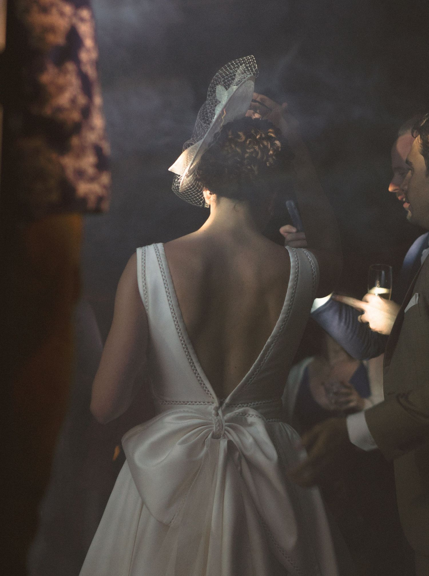 Fotografia da noiva dançando na festa com uma luz dramática, detalhe das costas e vestido branco com decote em V
