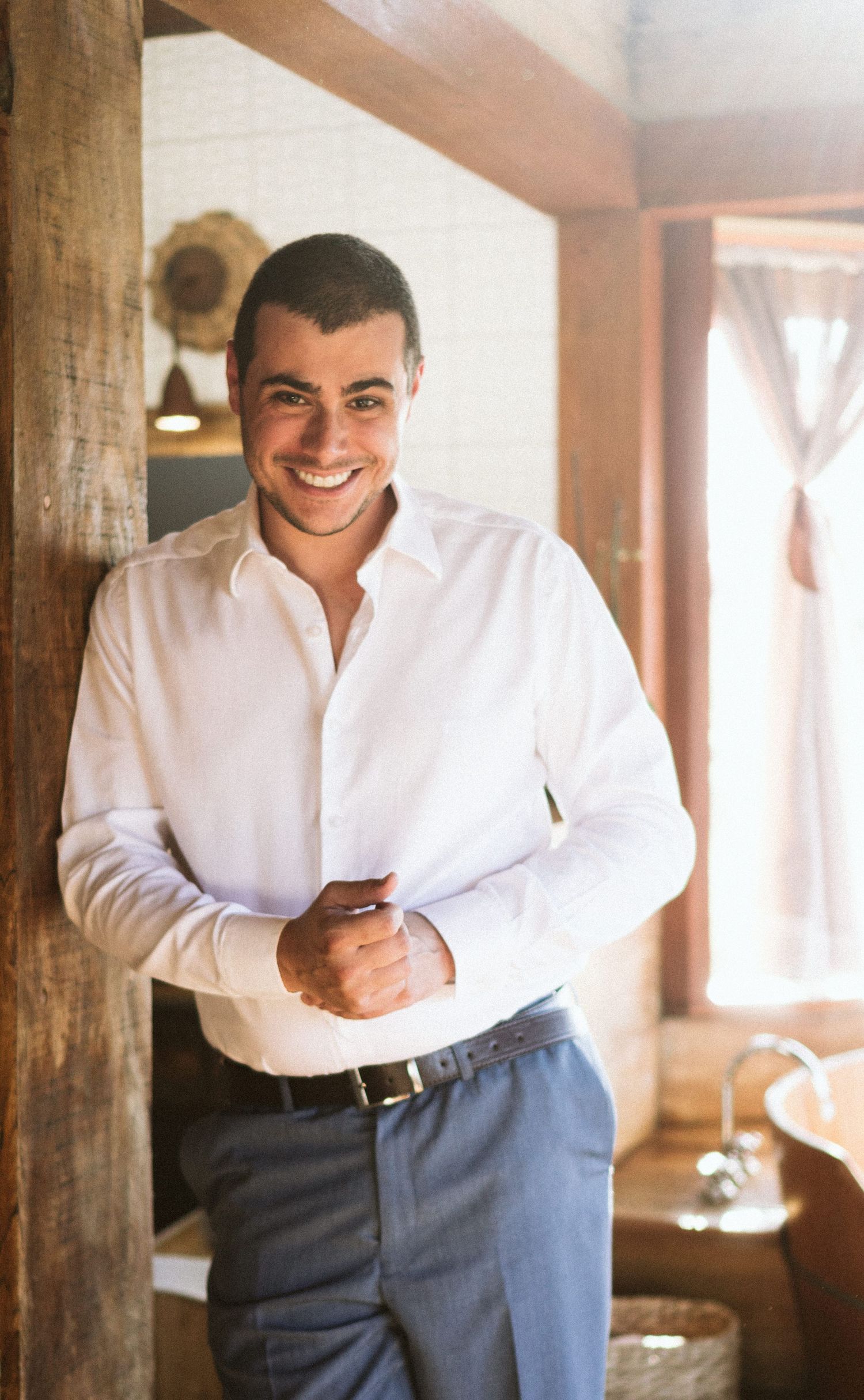 A person in formal attire smiling while standing in a rustic interior setting.