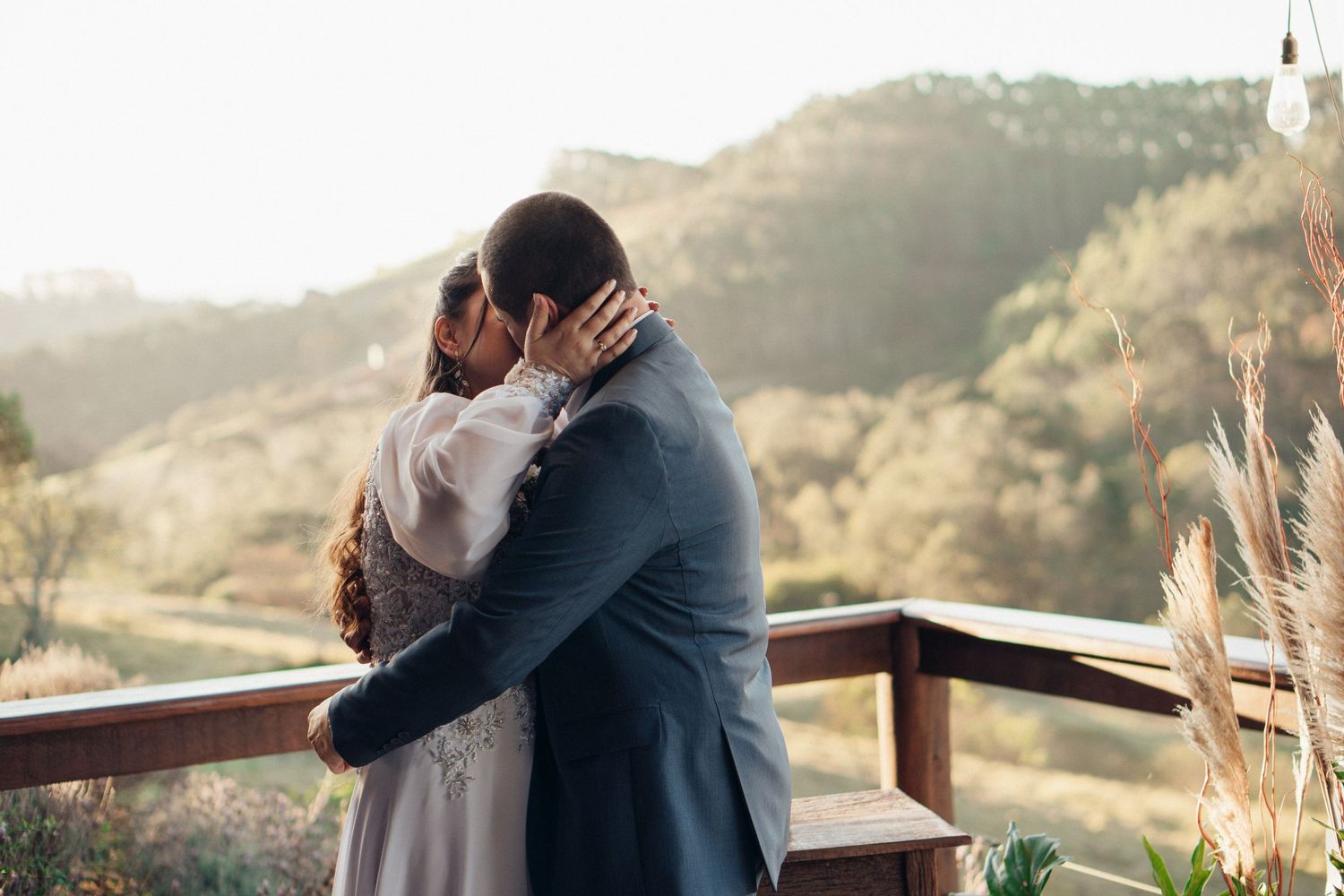 Abraço romântico entre o casal durante a cerimônia de casamento ao pôr do sol com montanhas ao fundo.