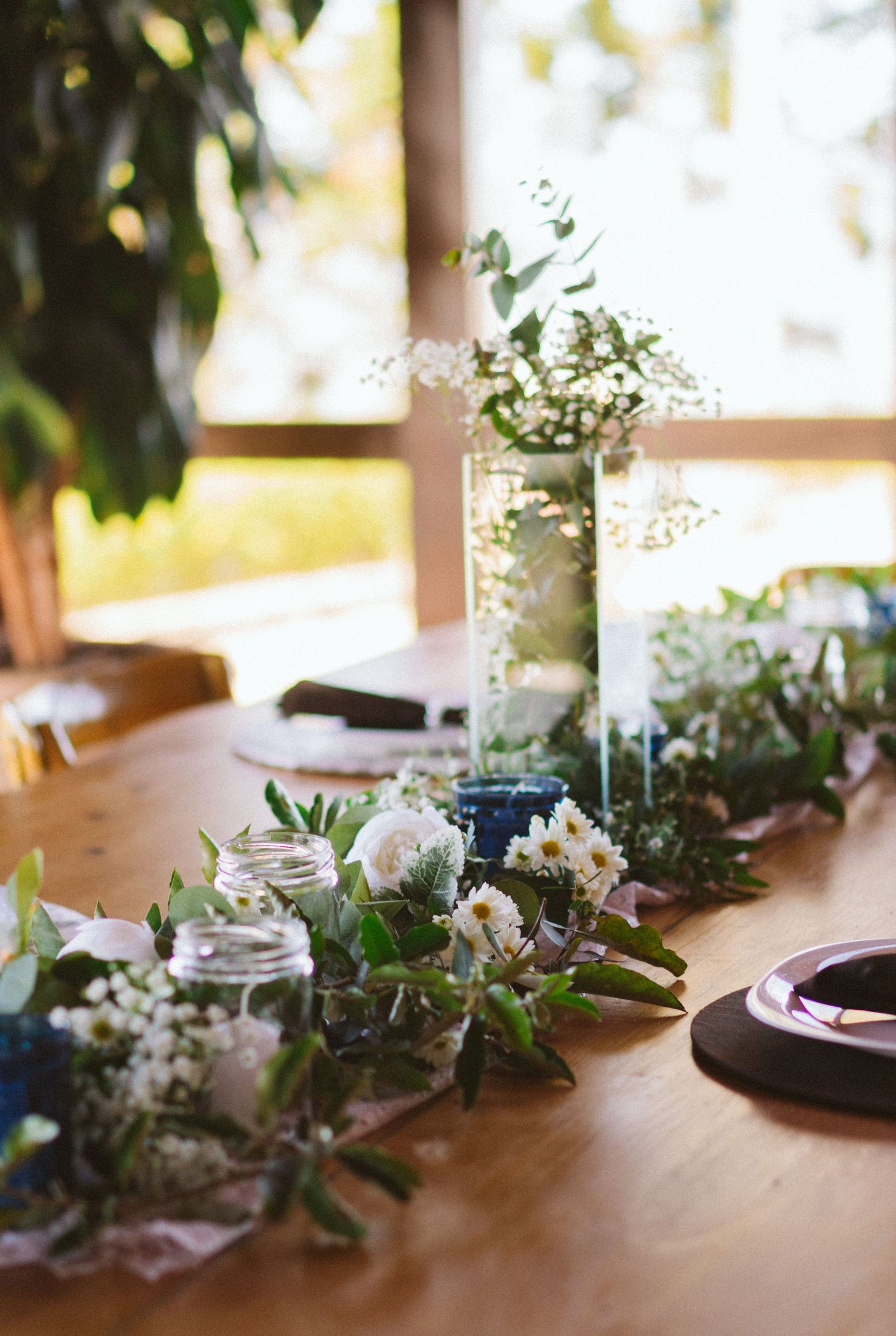 Rustic wedding table decoration with mason jars filled with baby's breath and greenery.