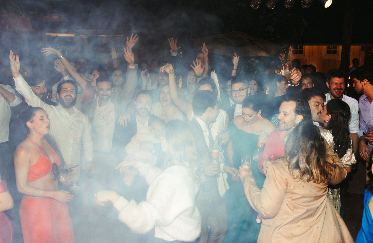 Convidados todos juntos durante festa de casamento dançando e pulando juntos entre as luzes coloridas e música animada, fotografia documenta