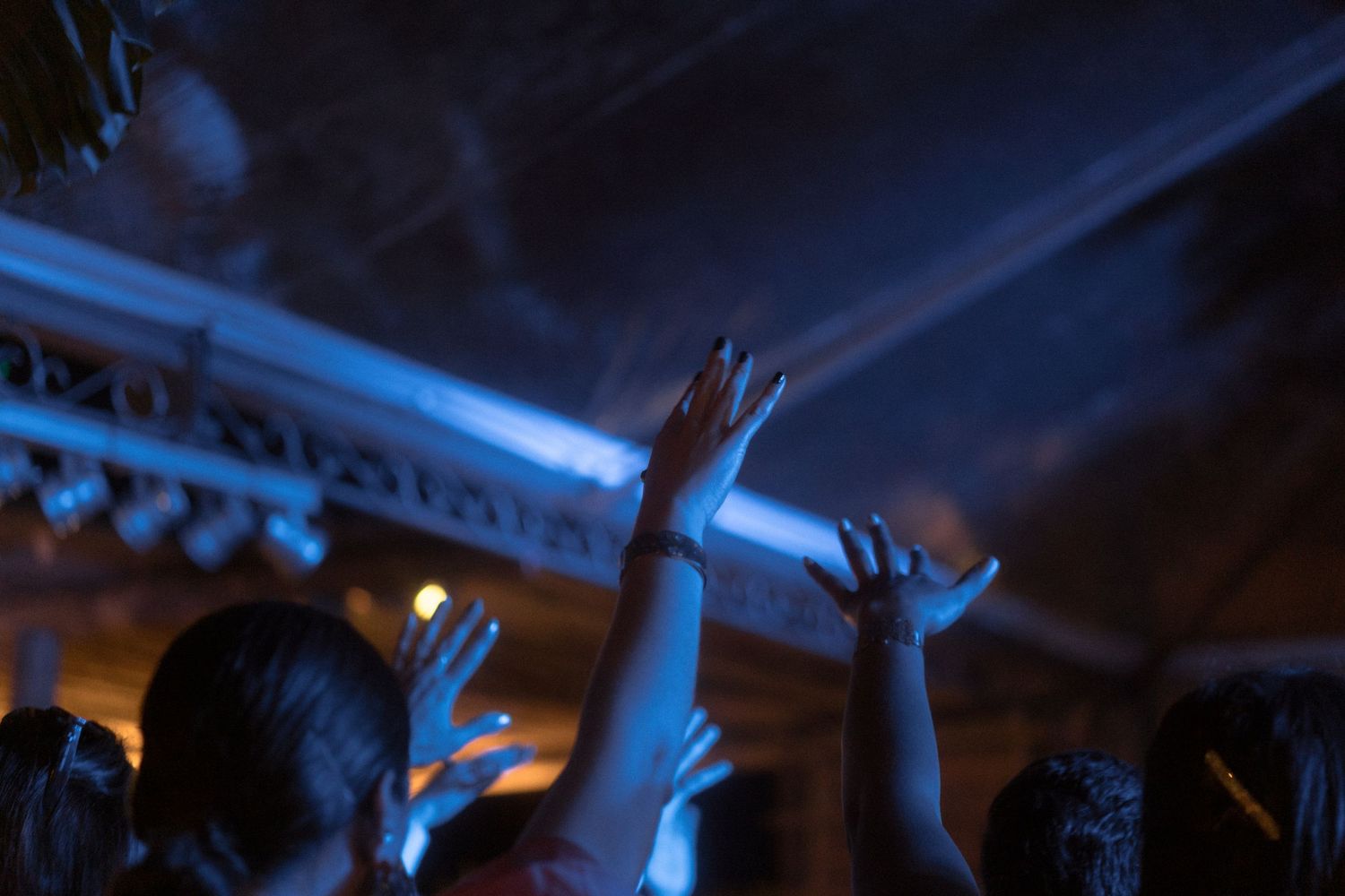 Convidados levantam as mãos e enquanto dançam em um casamento, criando uma atmosfera com iluminação azul no fundo