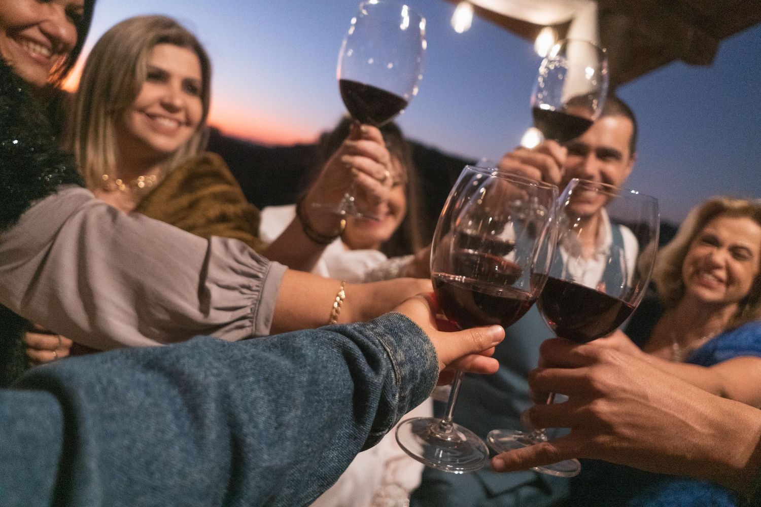 Amigos brindando com taças de vinho tinto durante a casamento ao pôr do sol.