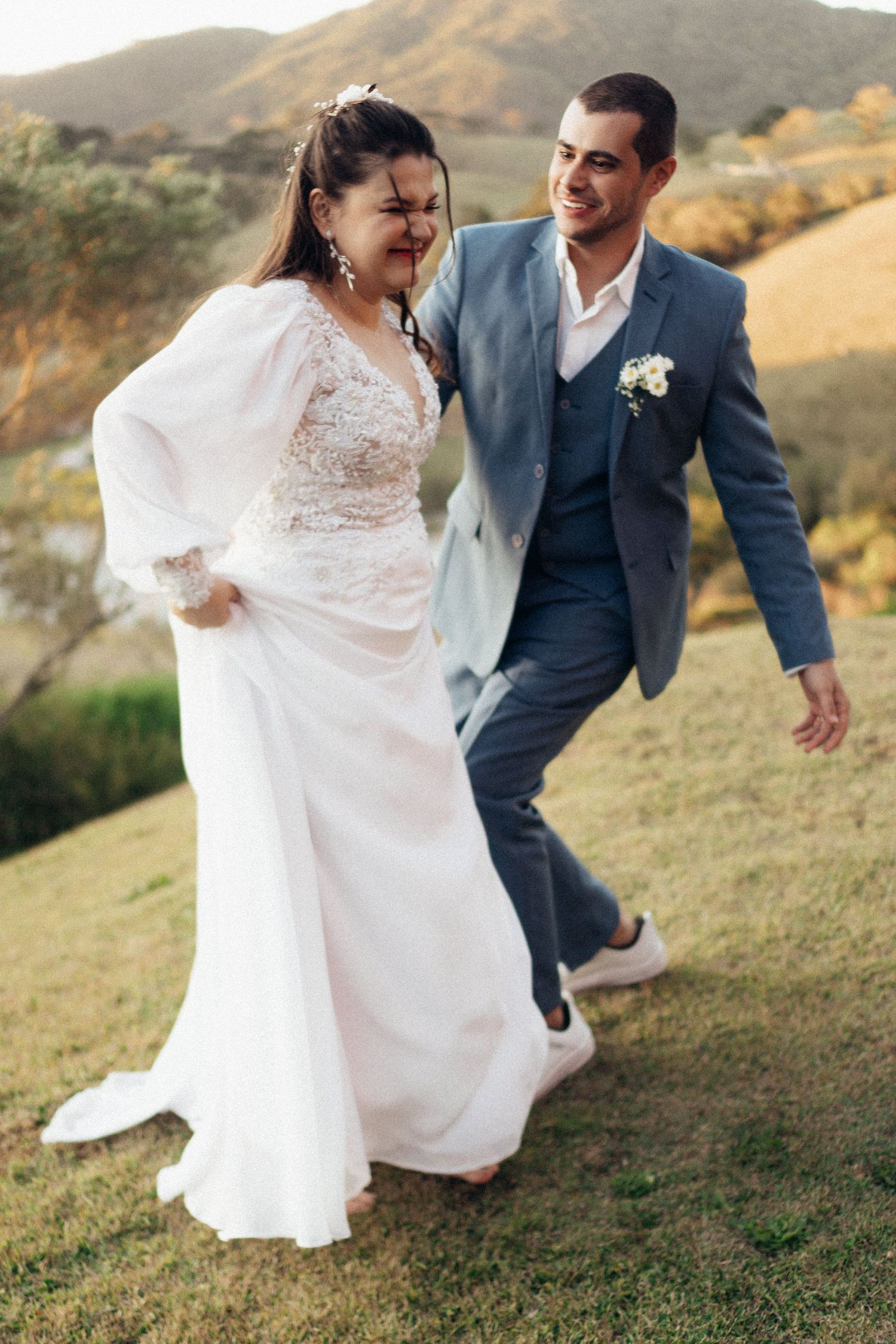 Recém-casados ​​riem juntos em uma encosta durante a sessão de fotos do casamento.