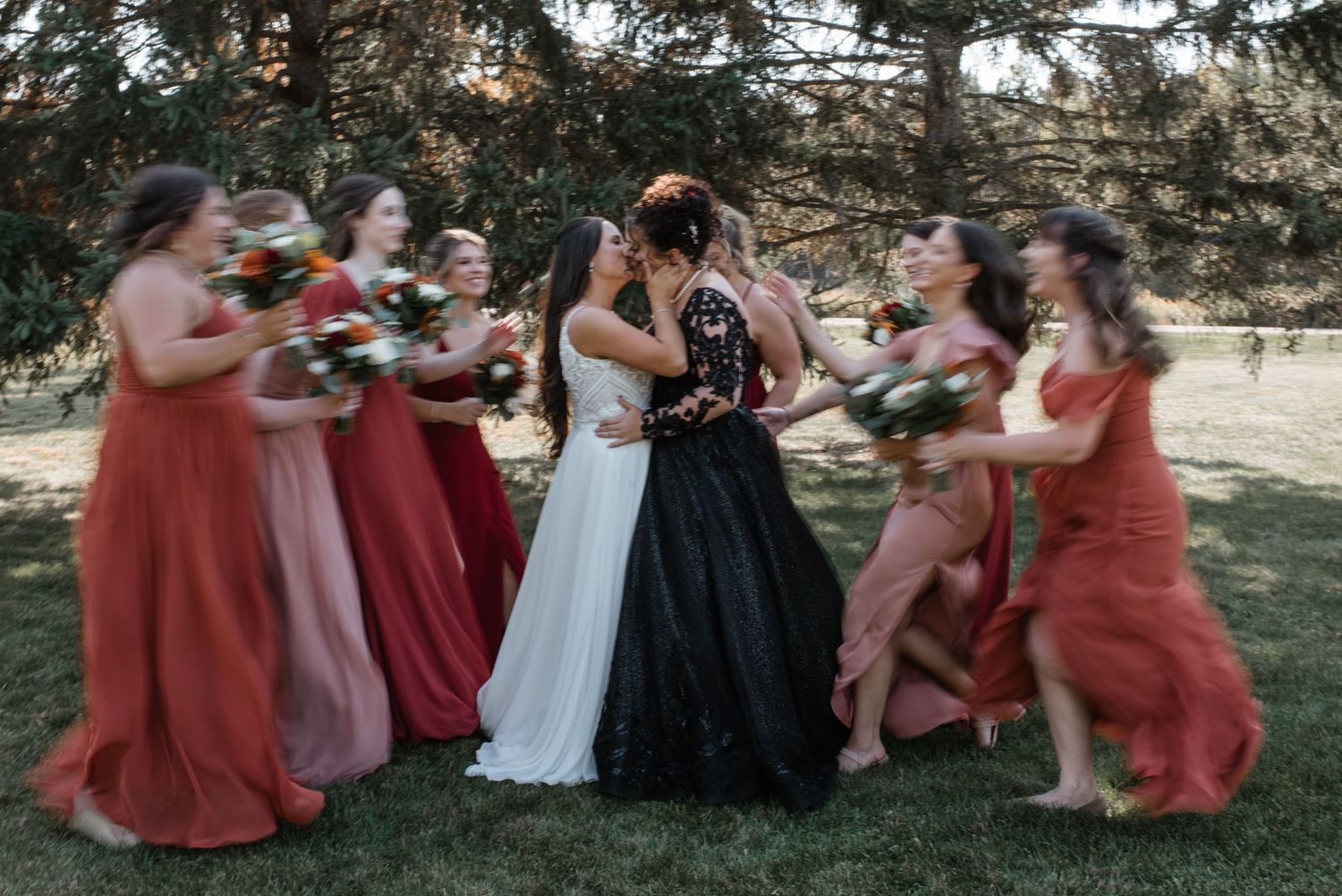 Wedding party in rust-colored dresses playfully pose together outdoors in a candid moment.