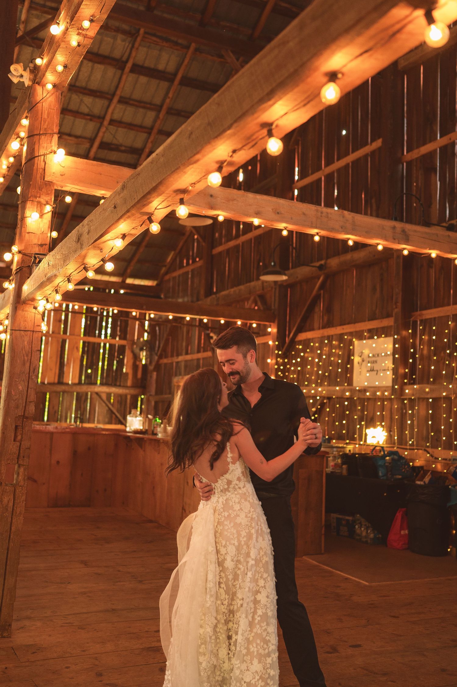 A romantic first dance moment captured in a rustic barn venue decorated with warm string lights and glowing ambiance.