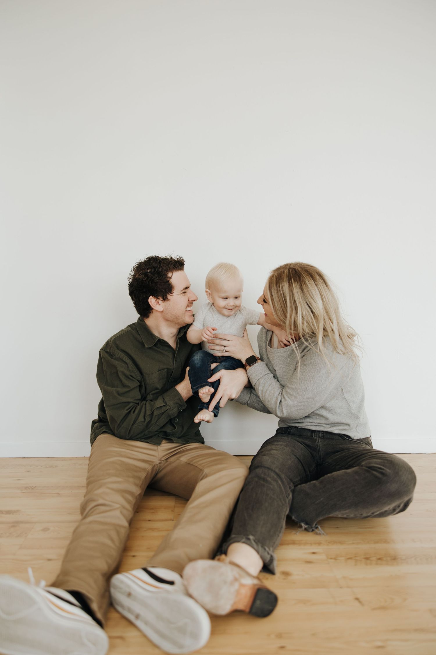A family sits together on a wooden floor sharing playful moments with their baby in a series of candid shots.