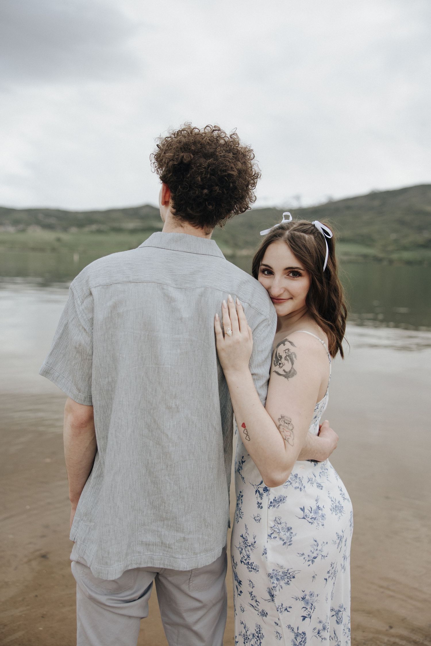 A couple shares tender moments together on a misty beach with mountains in the background.