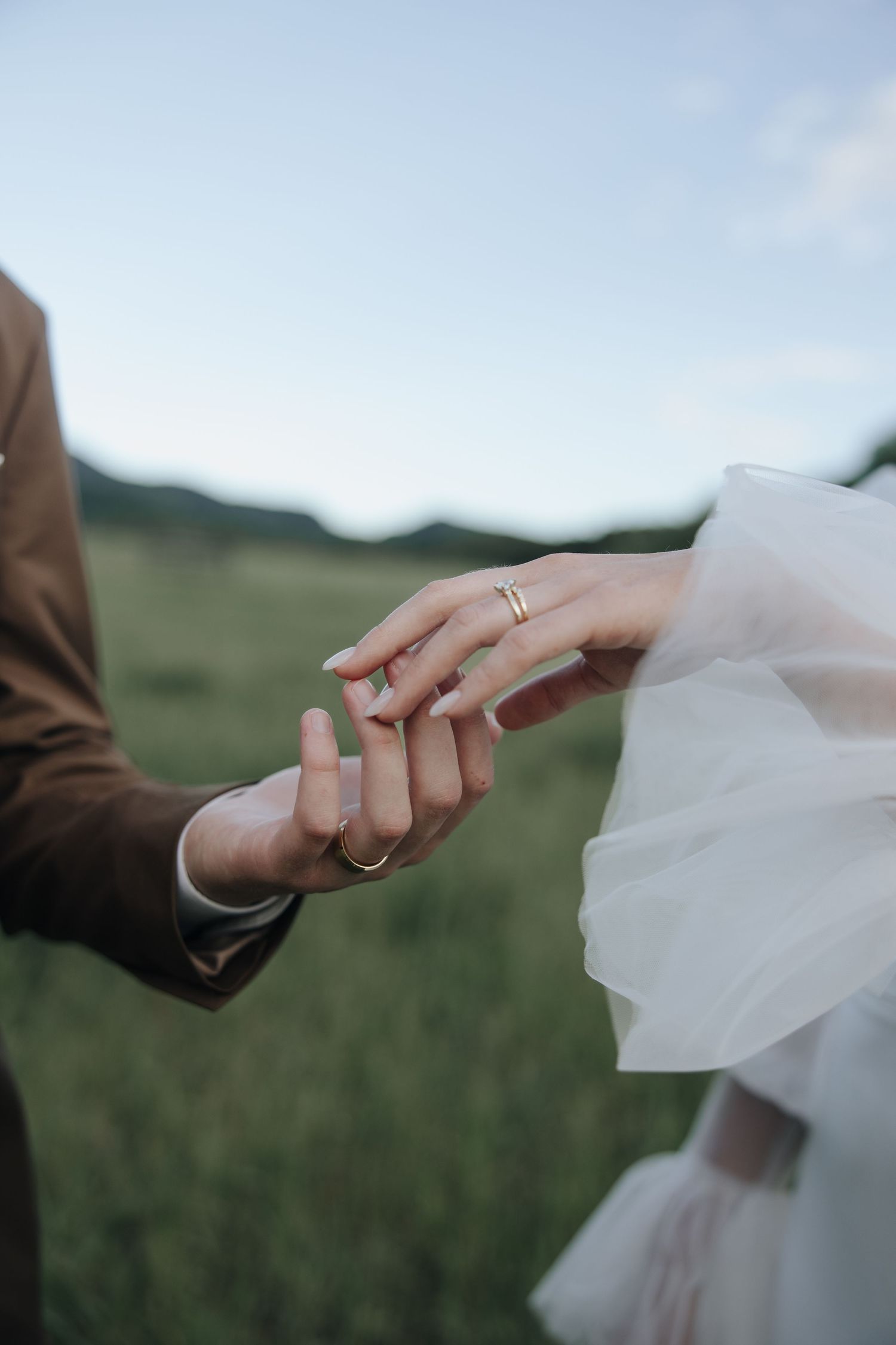 Close-up of hands displaying wedding rings against a mountainous backdrop.