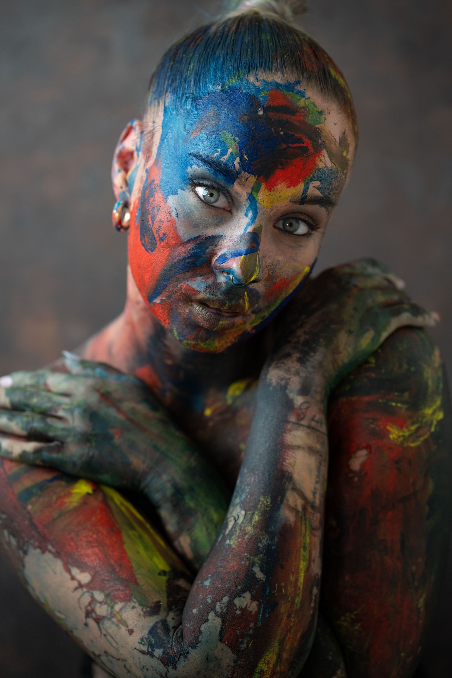 Woman covered in vibrant multicolored body paint poses with arms crossed, showcasing bold artistic expression.