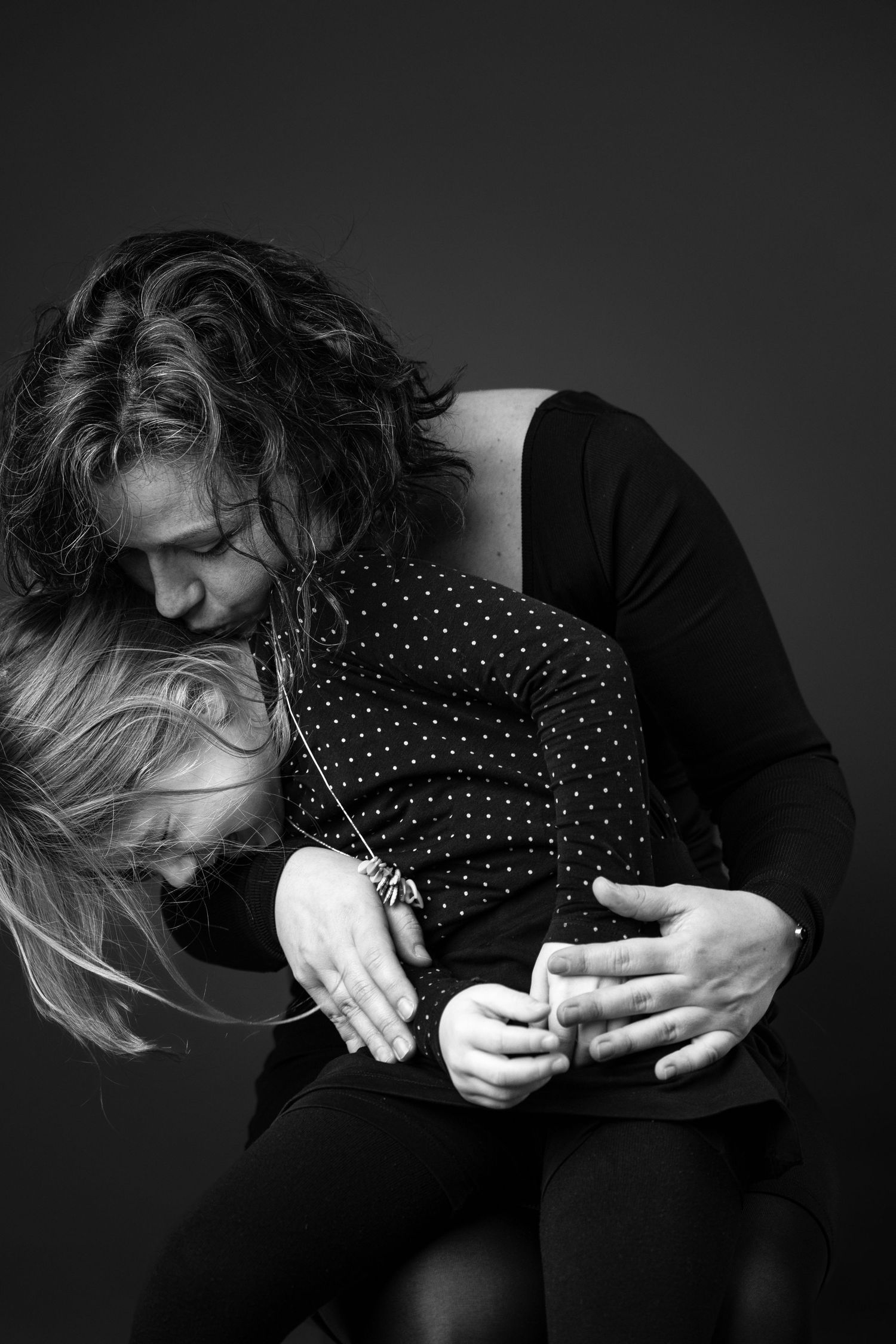 Black and white photo of a mother tenderly embracing her young child, both leaning together in an emotional moment.