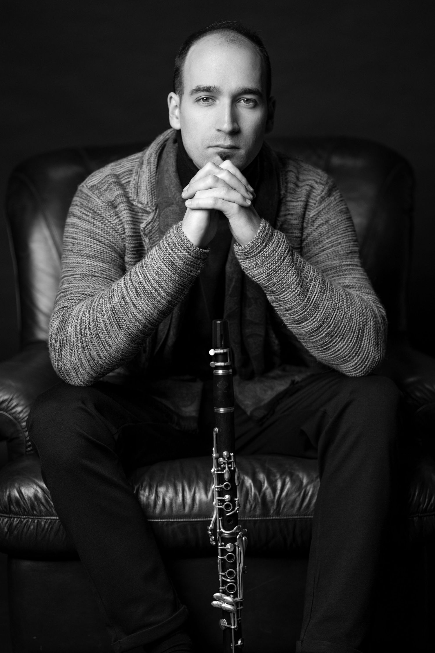 Black and white portrait of a man in a sweater sitting in a leather chair holding a clarinet.