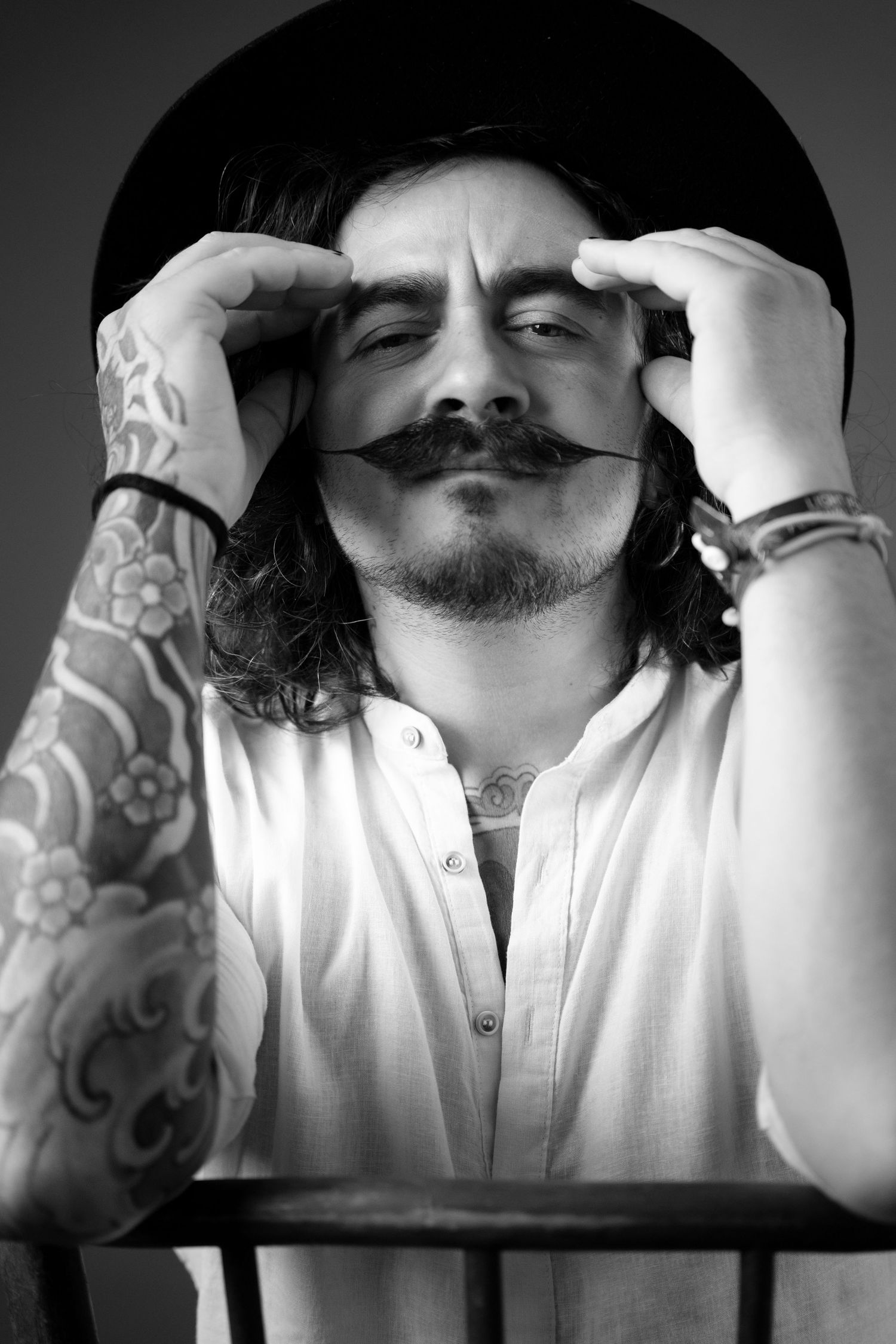 Black and white portrait of tattooed man with mustache wearing bowler hat and white shirt.