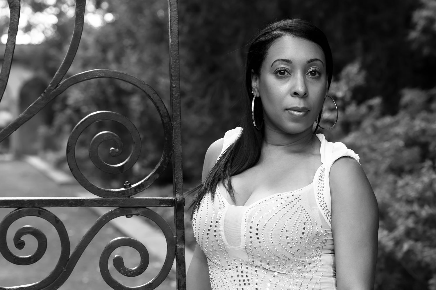 Black and white portrait showing woman in white lace dress by garden gate. Lifestyle photoshoot. L. Visions Photography