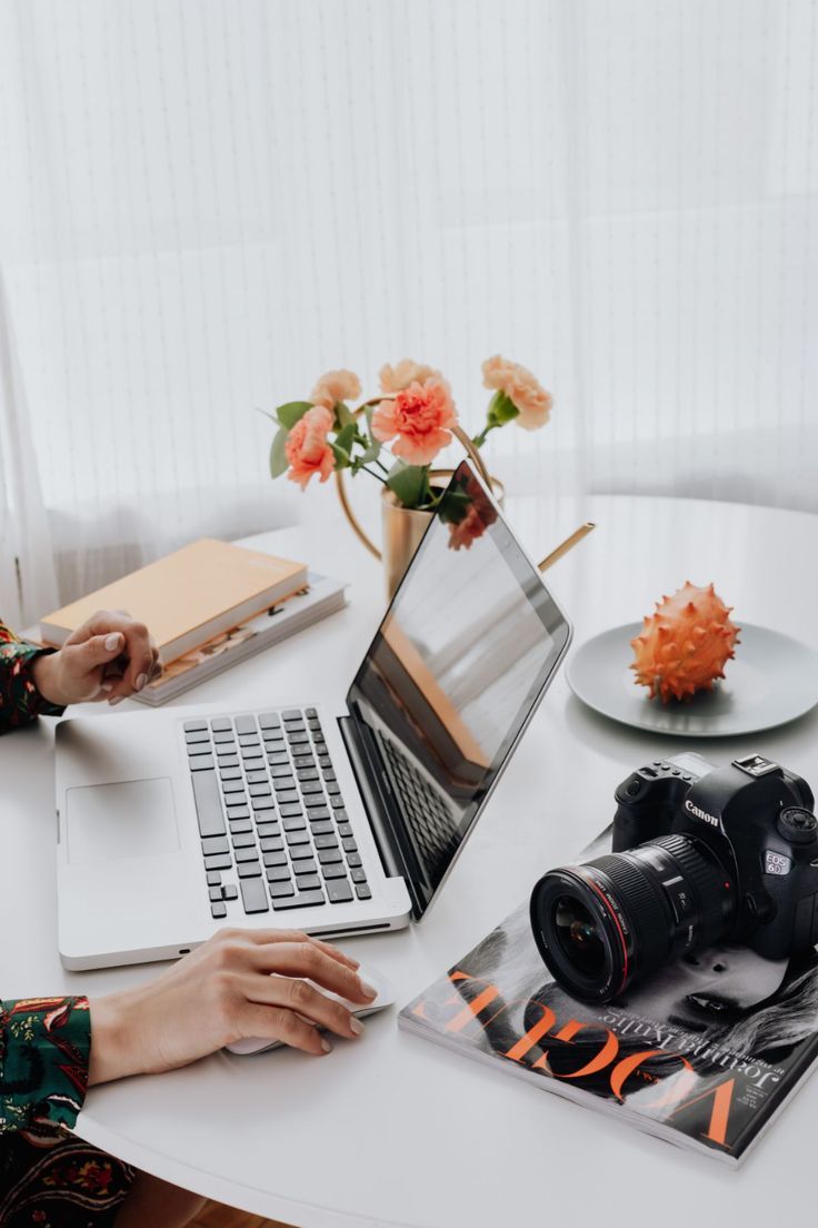 Desk scene with laptop, camera, flowers and hands typing in bright minimal workspace.  L Visions Photography