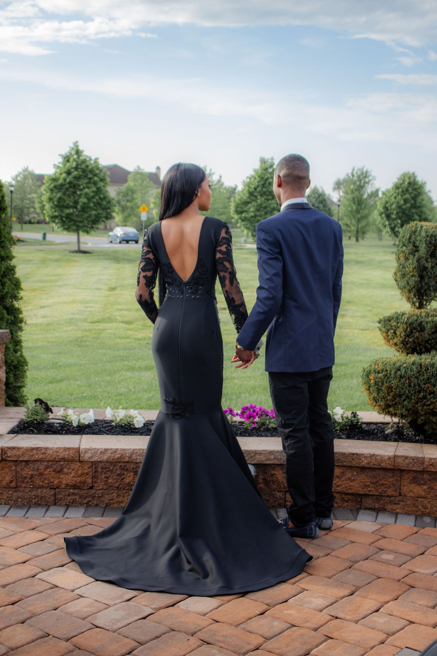 Couple in formal attire standing on brick patio with landscaped garden background. Prom photoshoot. L. Visions Photography
