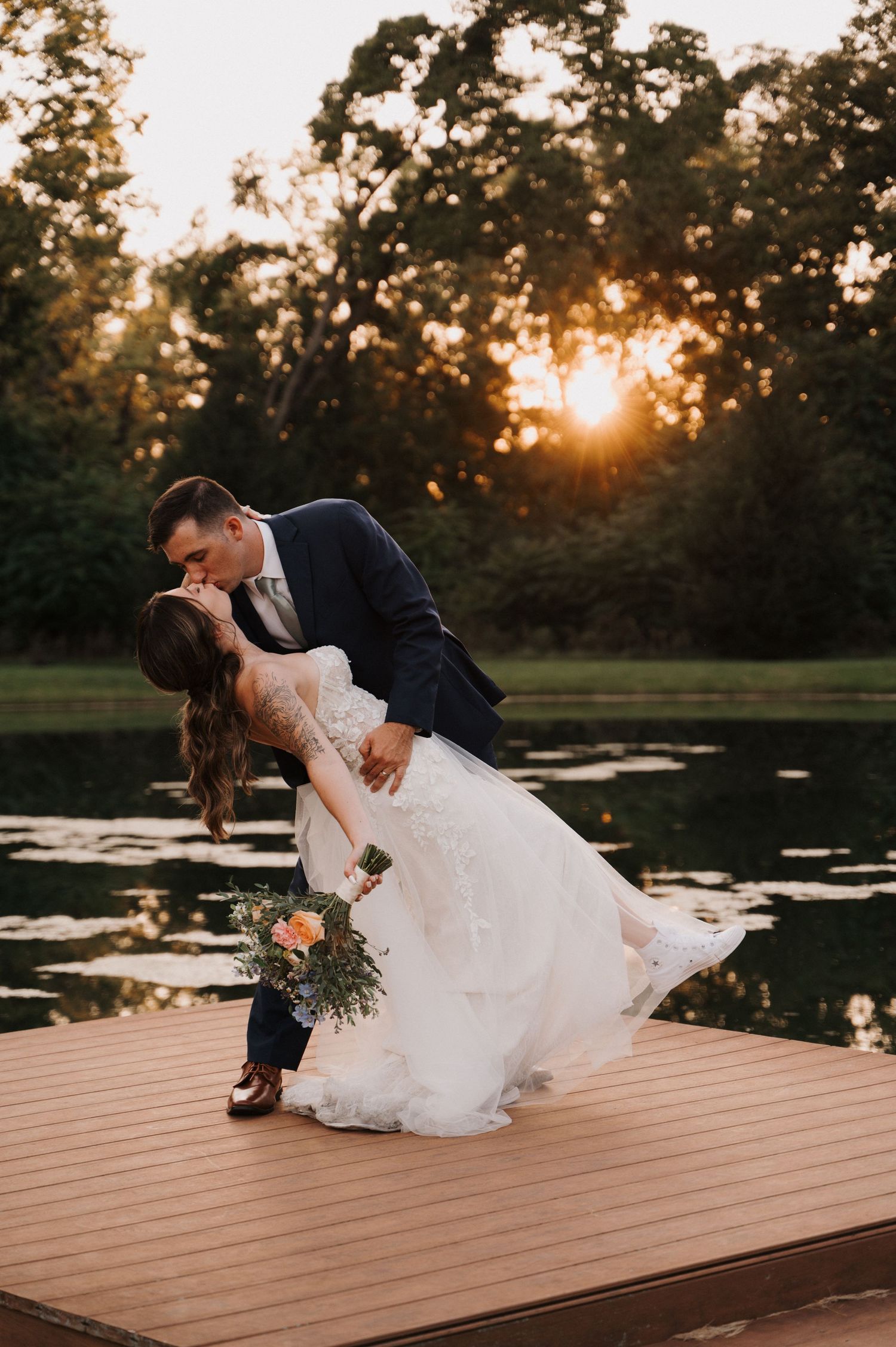 A romantic wedding couple shares a dip kiss on a dock at sunset with trees and water in the background in Cincinnati, Ohio