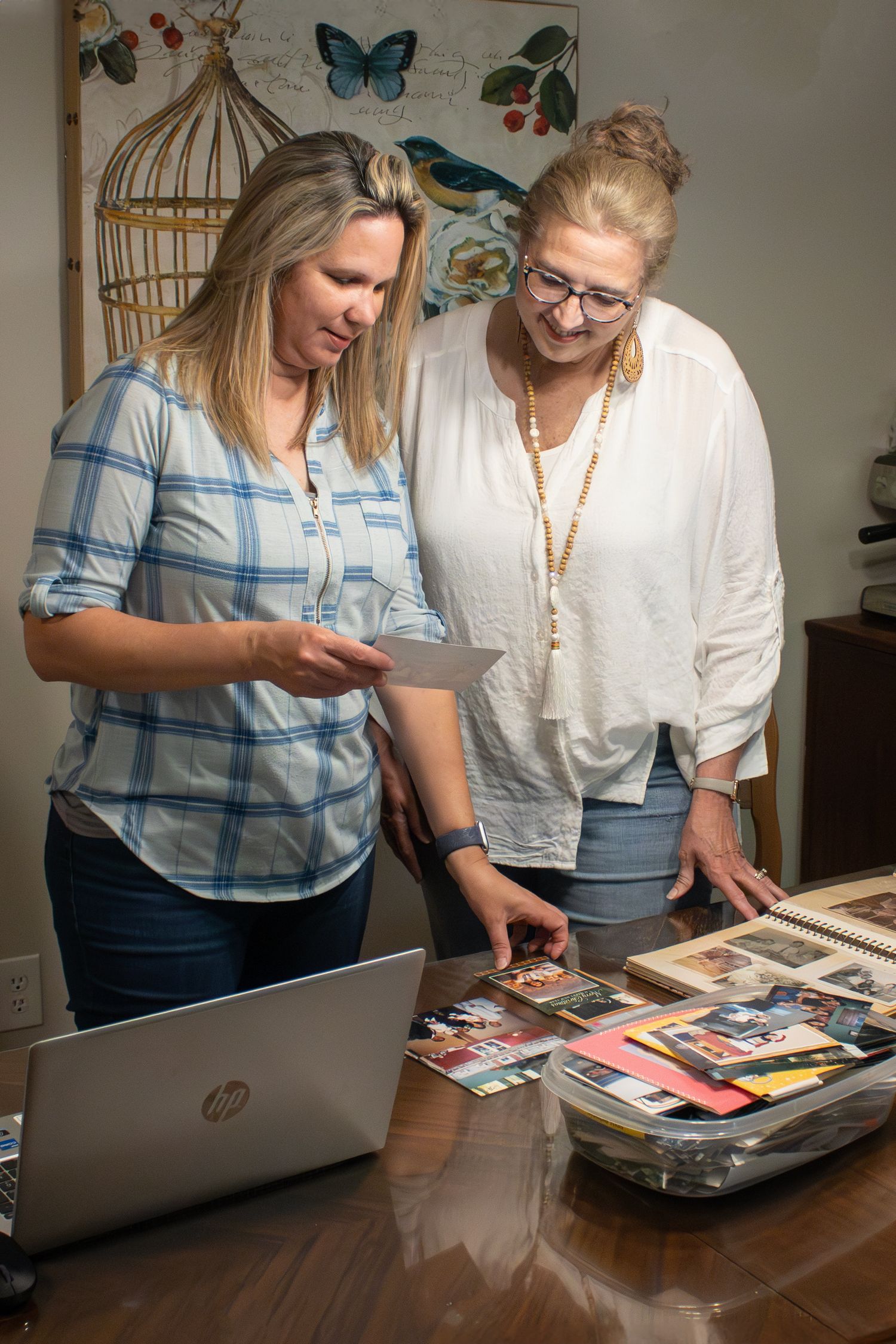 Two people looking over printed photos and digital photos on a laptop