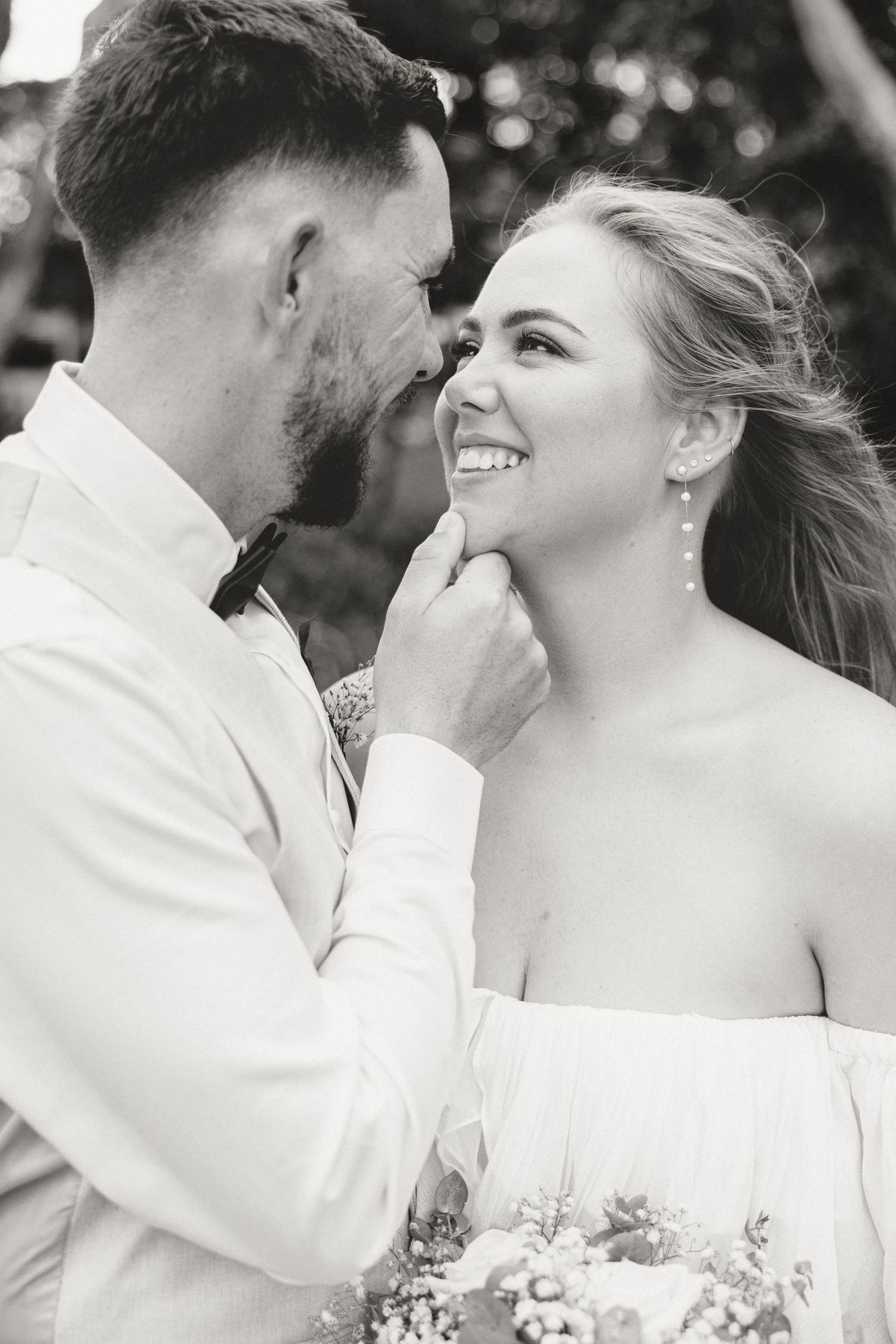 A romantic black and white wedding photo captures an intimate moment between a couple sharing laughter outdoors.
