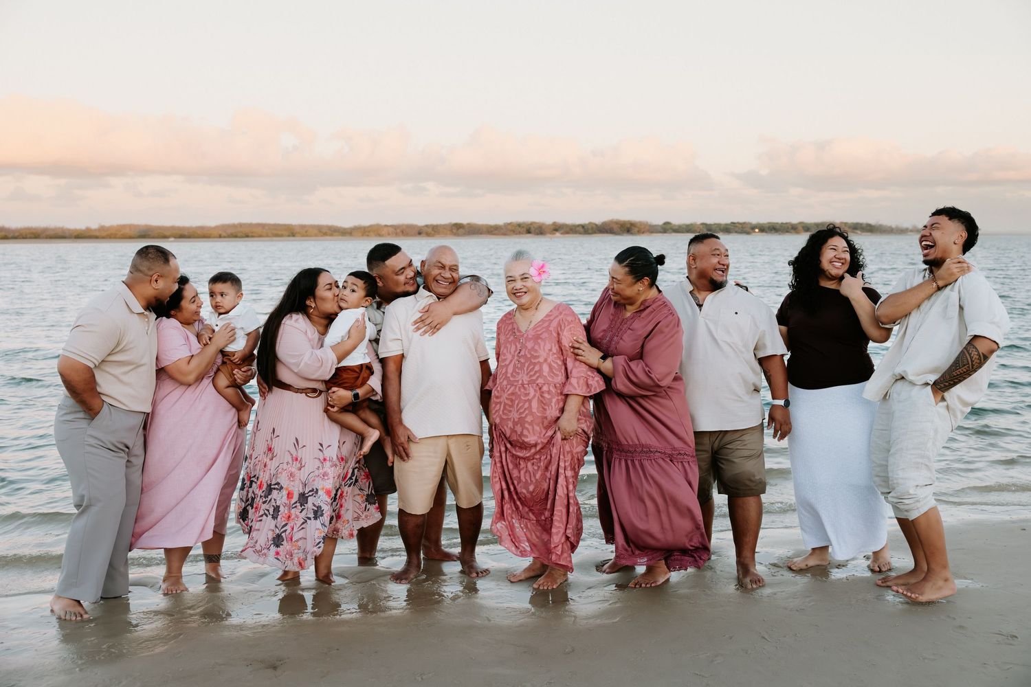 Group of people in coordinated pink and white outfits playing in ocean waves at sunset.