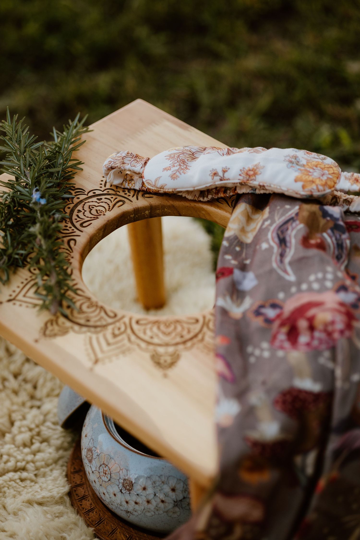 Wooden meditation table with mandala engravings, herbal eye pillow, floral scarf, and ceramic bowl on a cozy blanket.