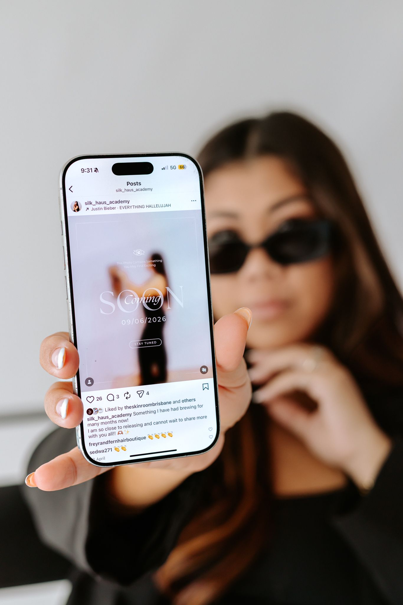 Woman in sunglasses holding smartphone displaying Instagram post in a modern minimalist setting.