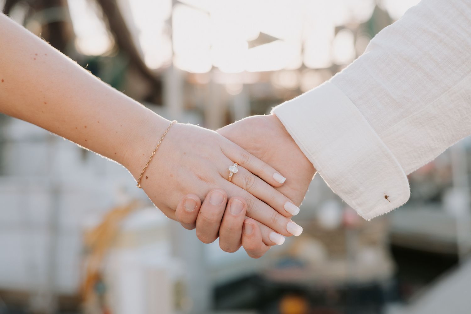 Close-up of a couple holding hands, woman wearing a gold bracelet and engagement ring with white manicured nails.