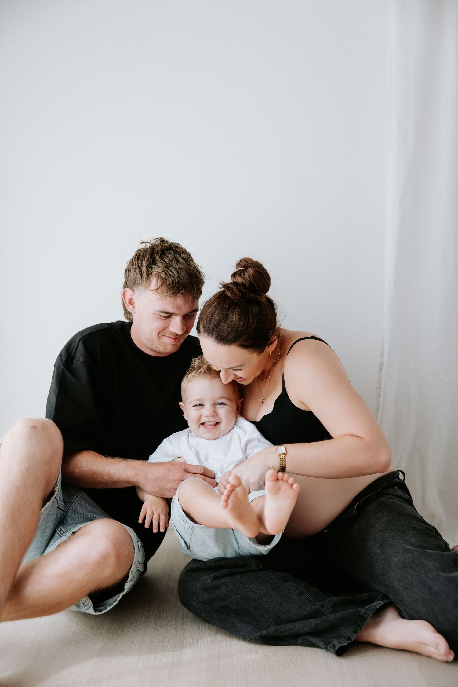 A family shares tender moments together while relaxing on a white floor in matching black outfits.