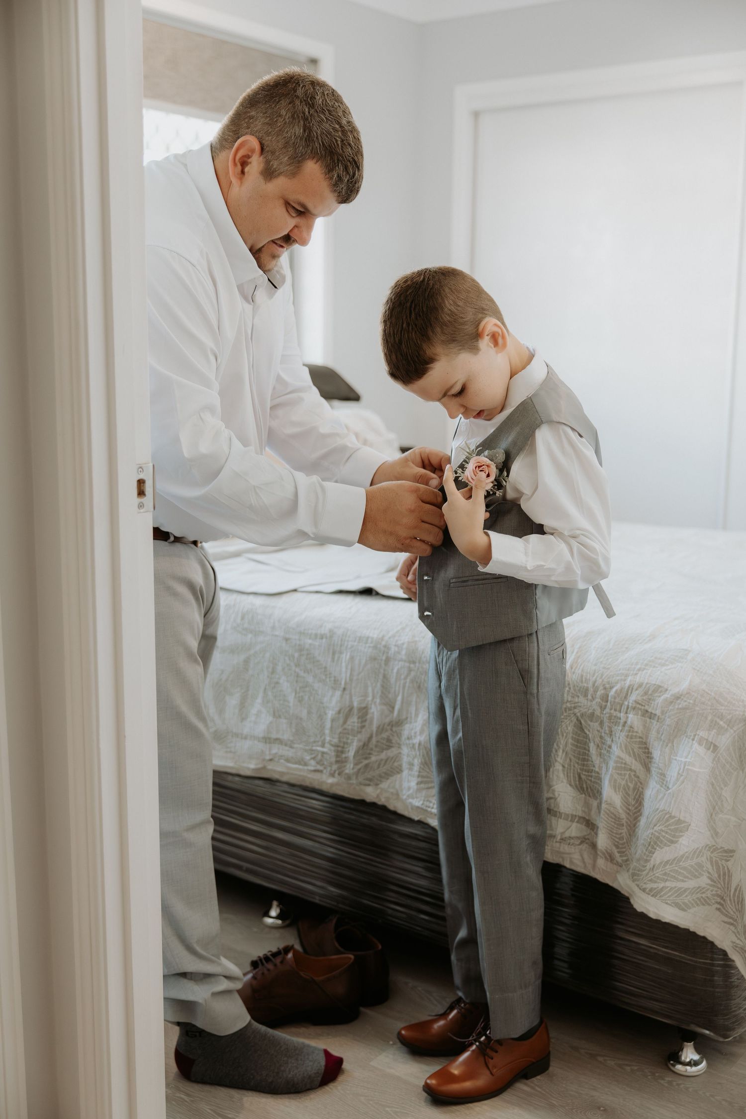 Tender moment of helping with formal attire preparations in bedroom setting.