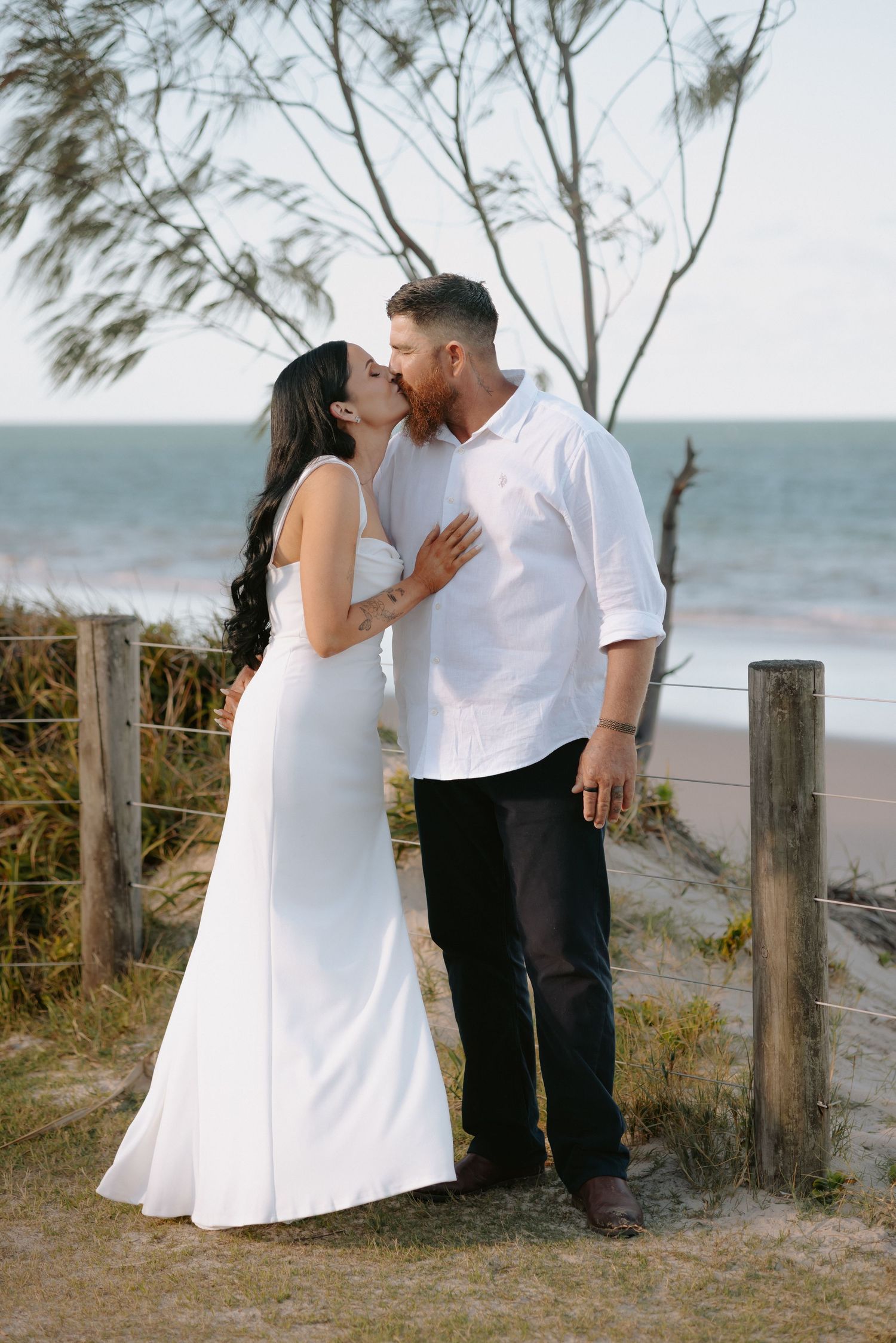 A couple embracing on a coastal path with ocean and trees in background.