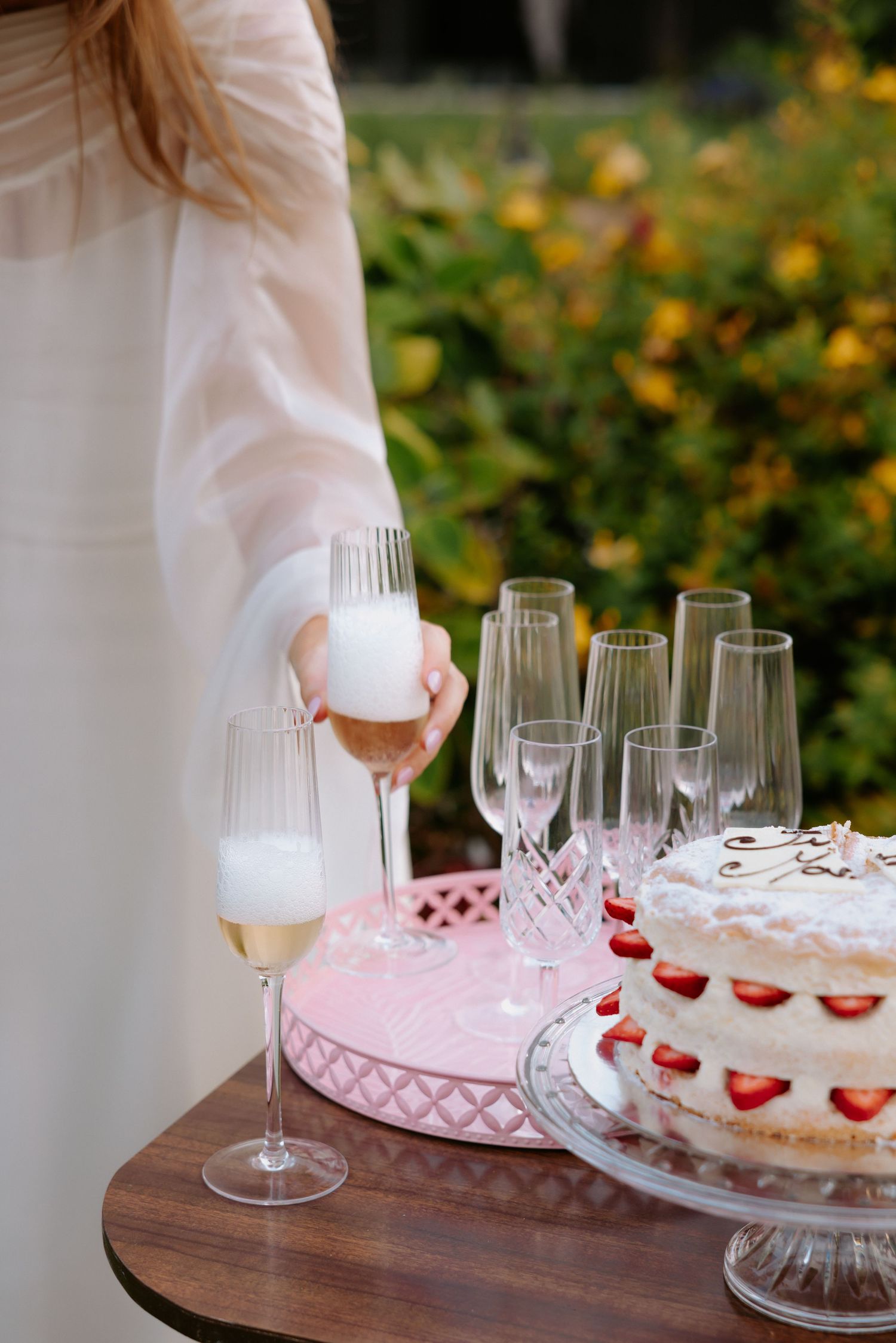 Wedding reception table with champagne glasses and a pink and white decorated cake.