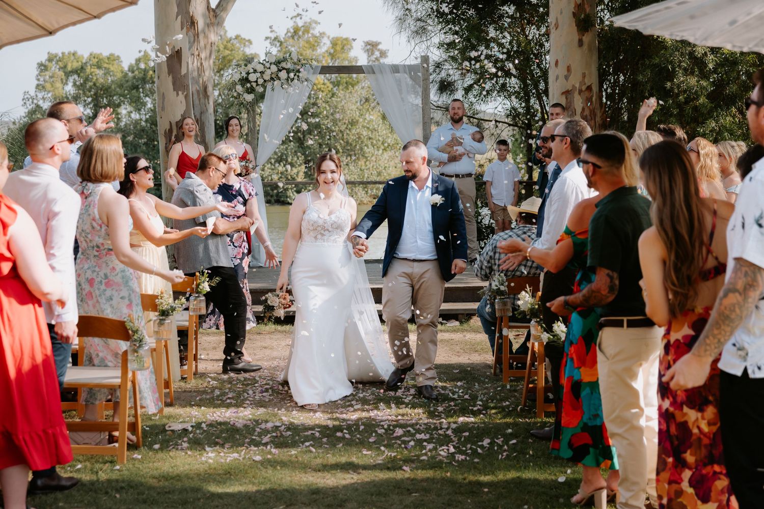 Wedding guests celebrating under trees with confetti in the air.