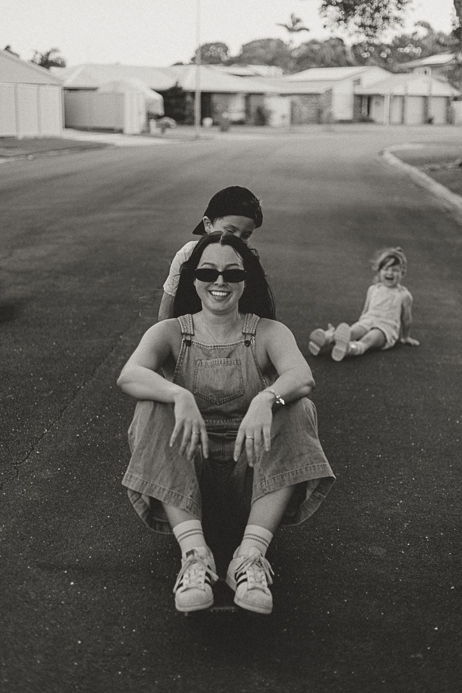 Black and white photo series showing someone sitting on pavement wearing sunglasses and overalls in different poses.