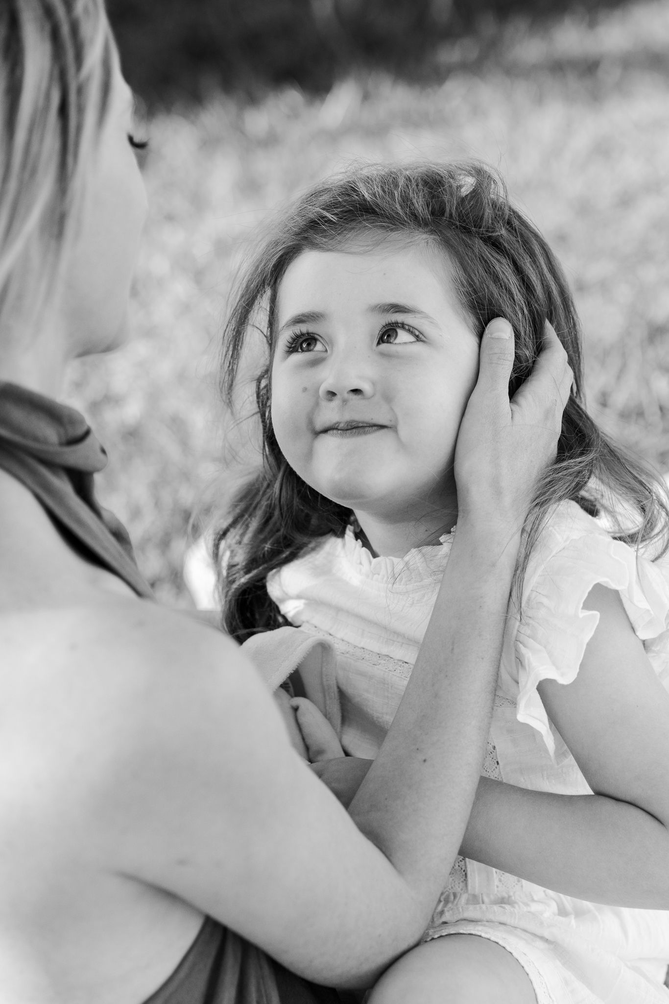 Black and white photo of a woman tenderly holding a young girl's face as she looks up smiling outdoors.